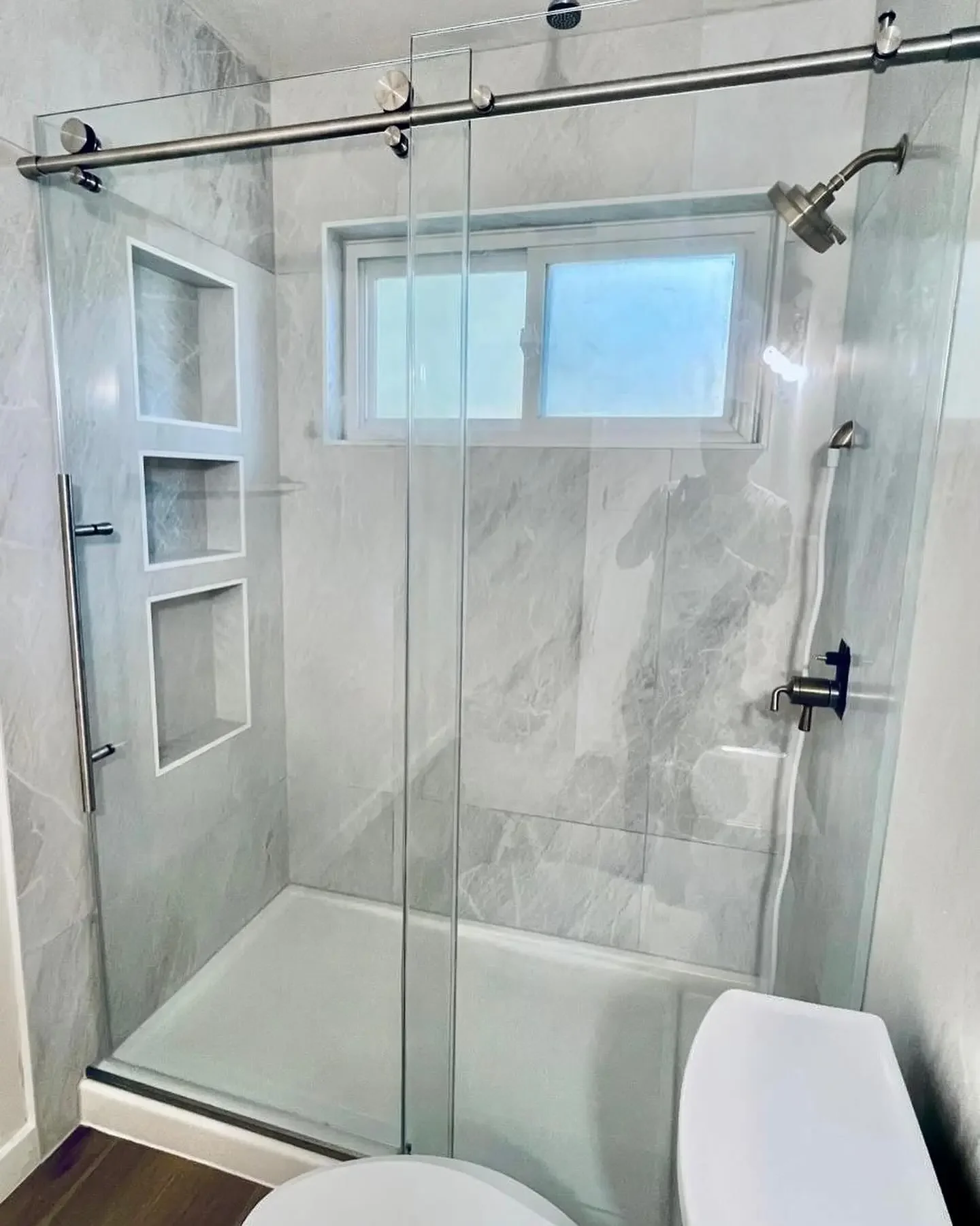 Bathroom shower with glass doors, built-in shelves, frosted window, and handheld showerhead.