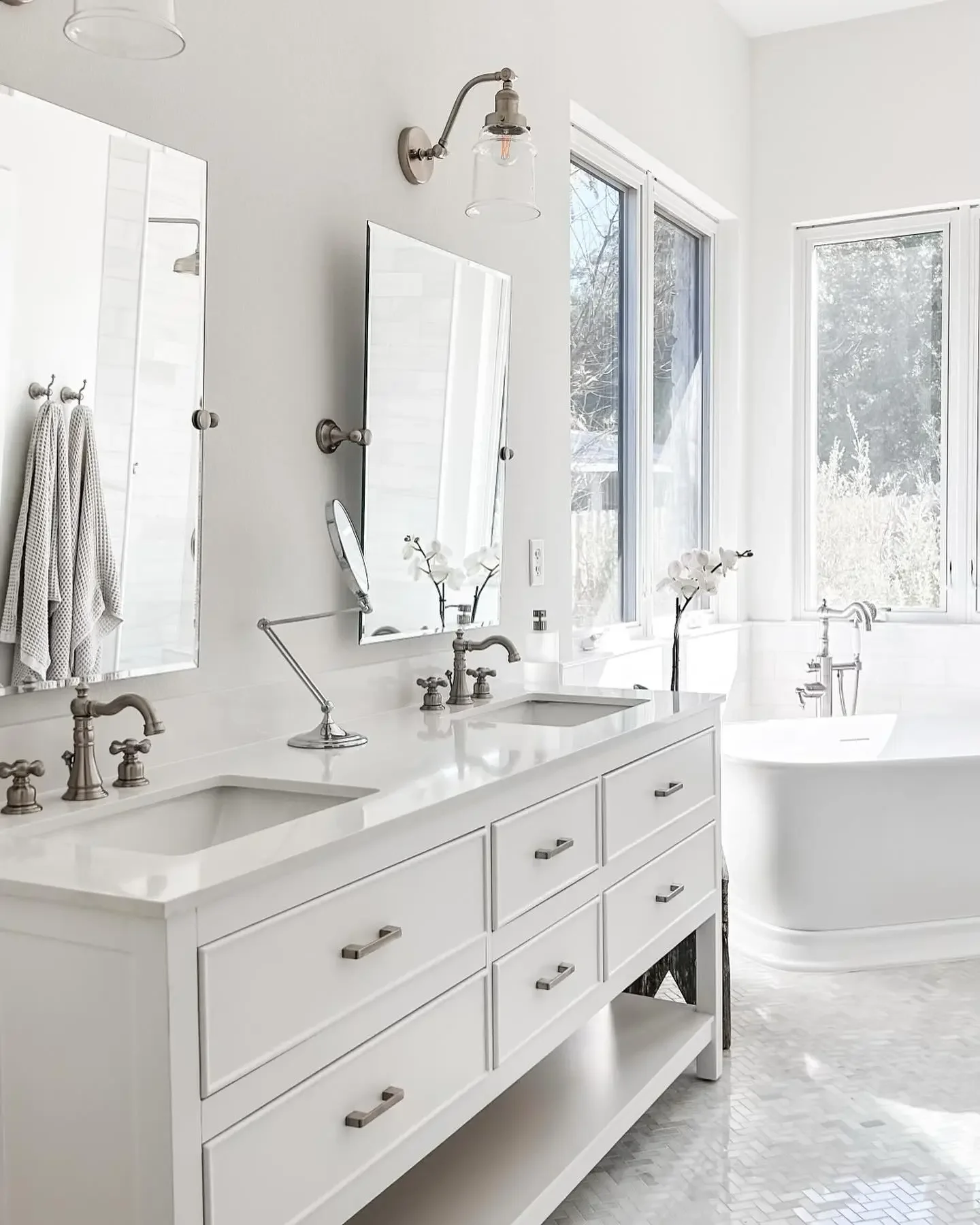 Bright white bathroom with double vanity and large window, with a bathtub in the corner.