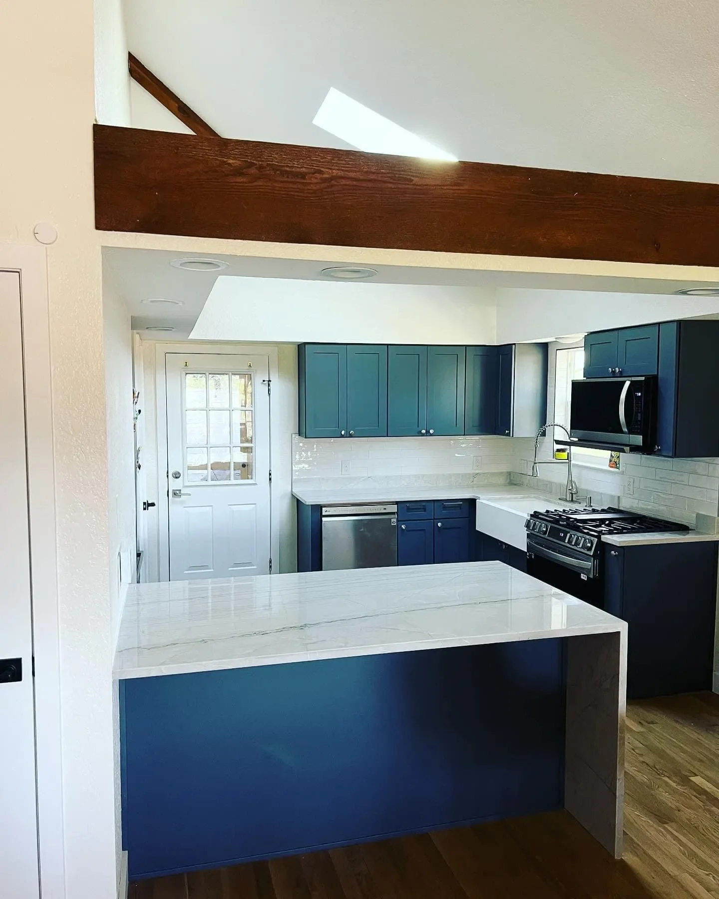 Kitchen with blue cabinets, white marble countertops, a white farmhouse sink, black appliances, and a wooden beam across the ceiling.