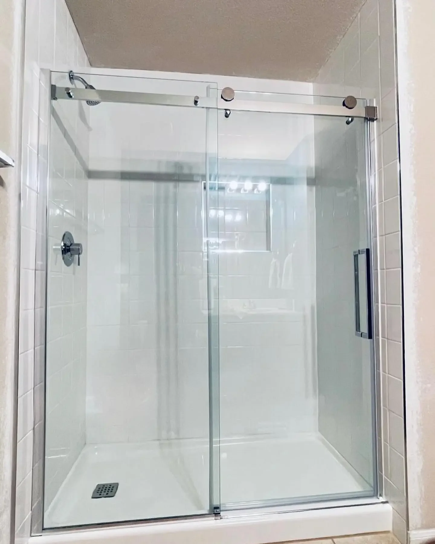 A modern walk-in glass shower with sliding doors, a chrome shower head, and tiled walls.