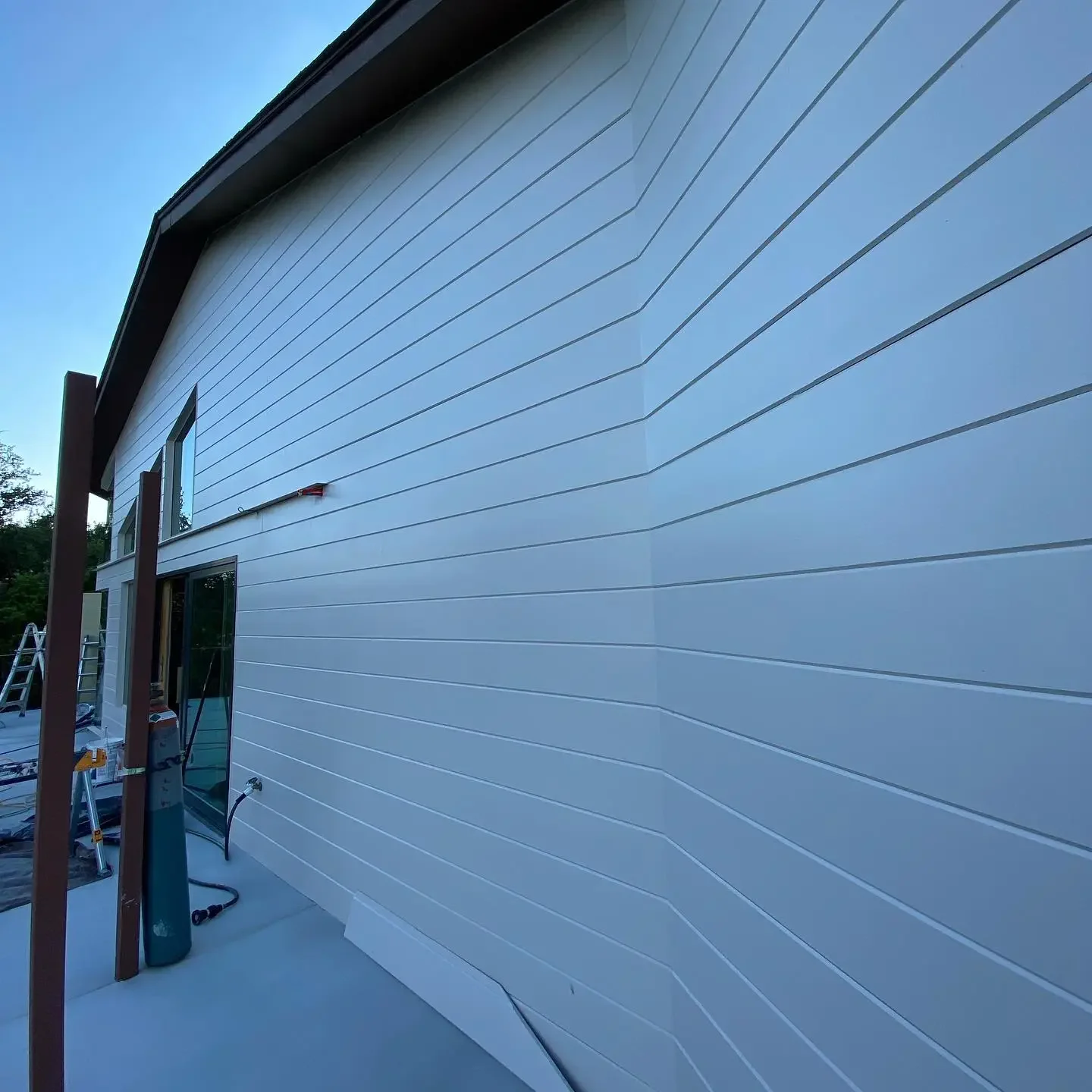 View of a house exterior with white siding, two windows, and construction tools nearby on the ground.