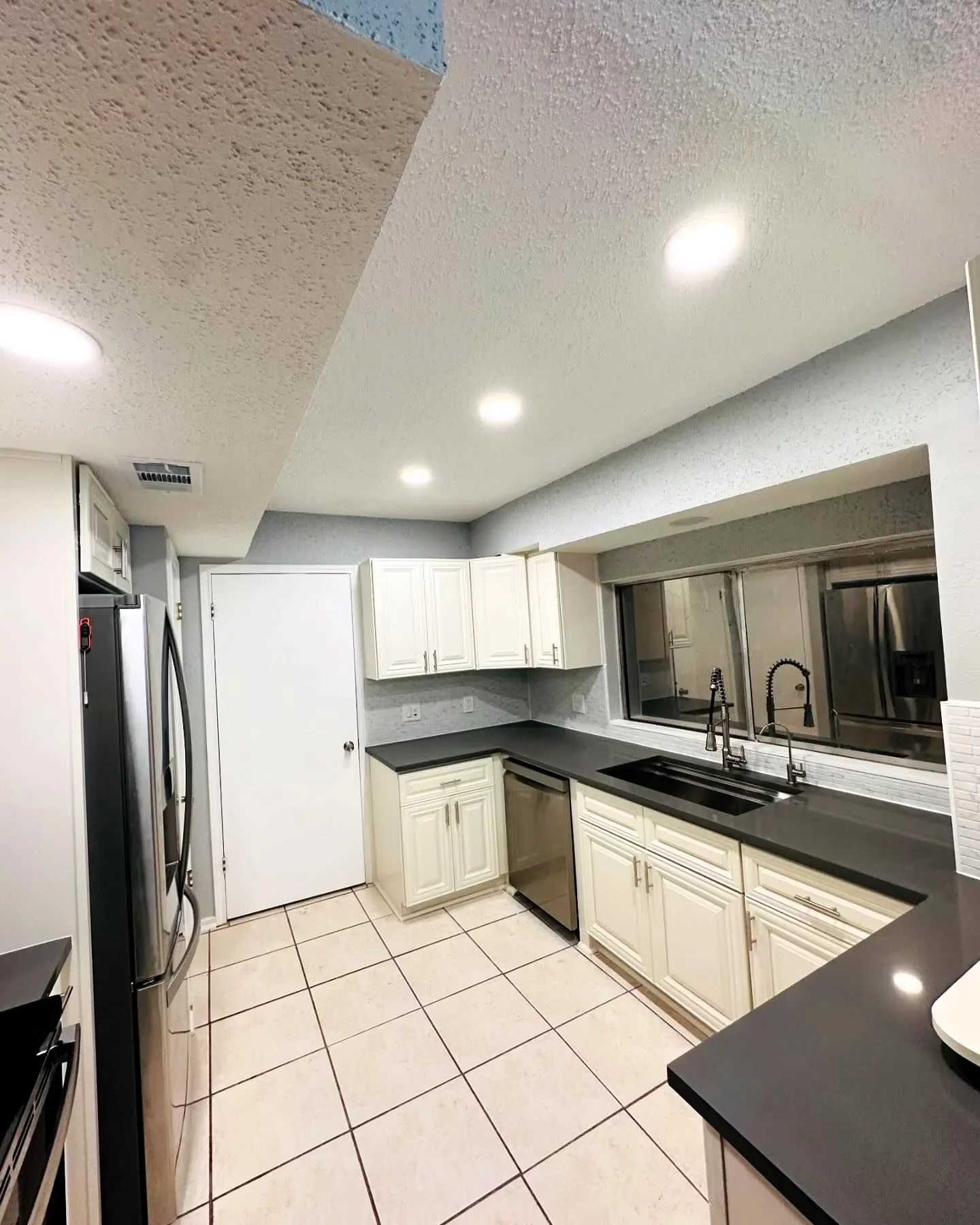 Kitchen with white cabinets, black countertops, stainless steel appliances, tiled floor, and a large window above the sink.
