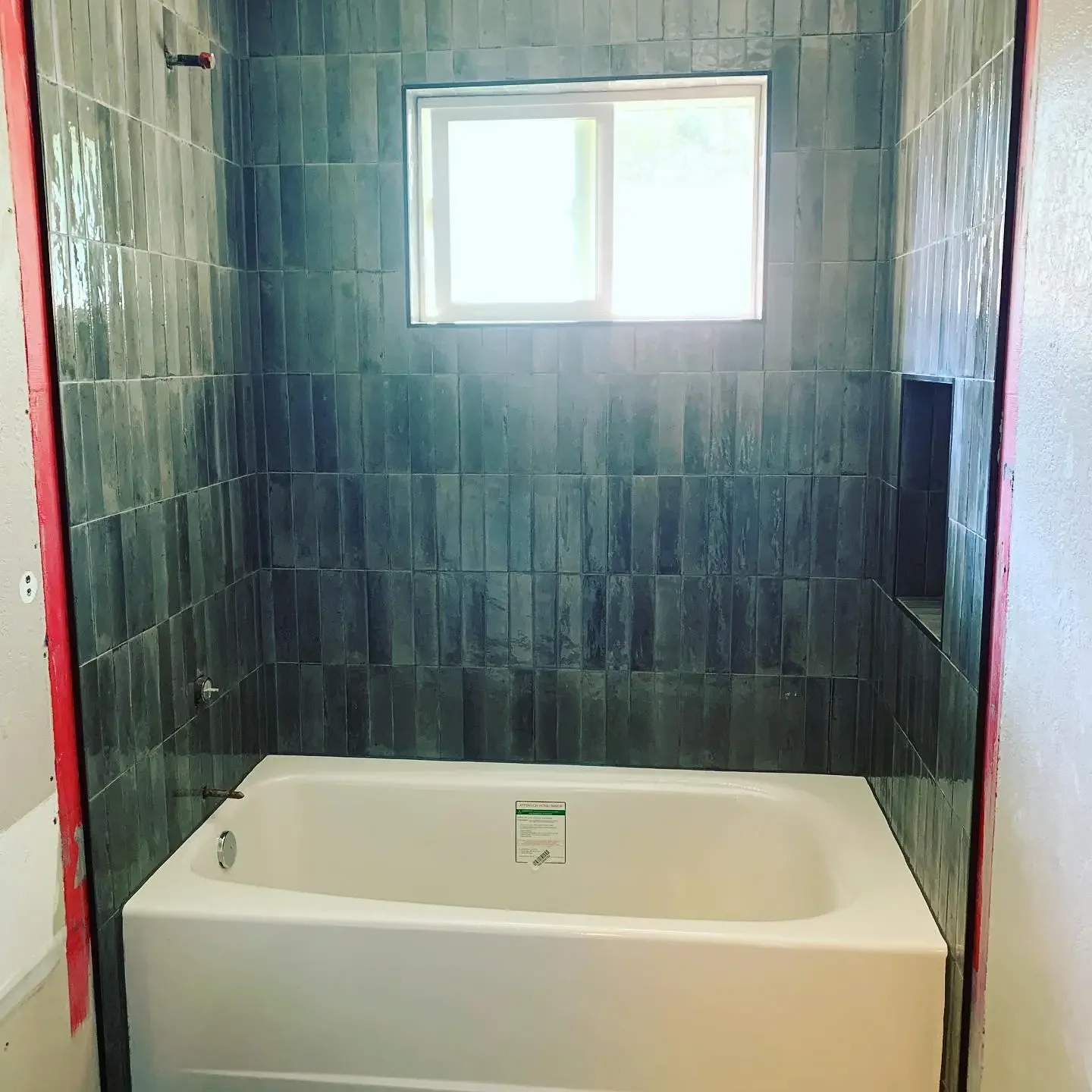 Bathroom with green tiled walls, a bathtub, and a small window letting in natural light.