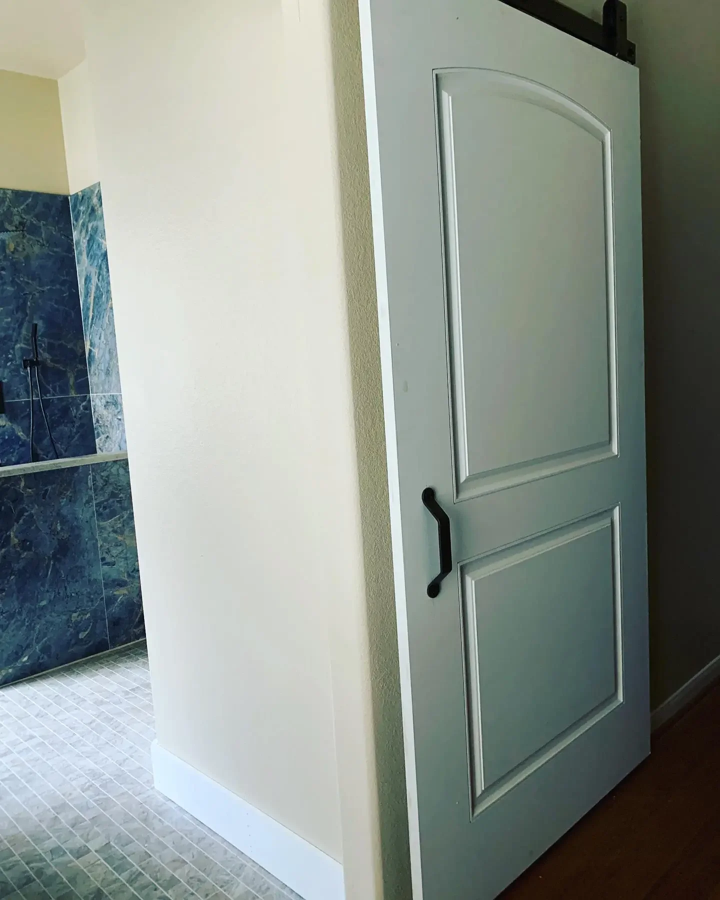 A white interior door partially open, revealing a bathroom with blue marble tiles and a walk-in shower with a handheld showerhead.