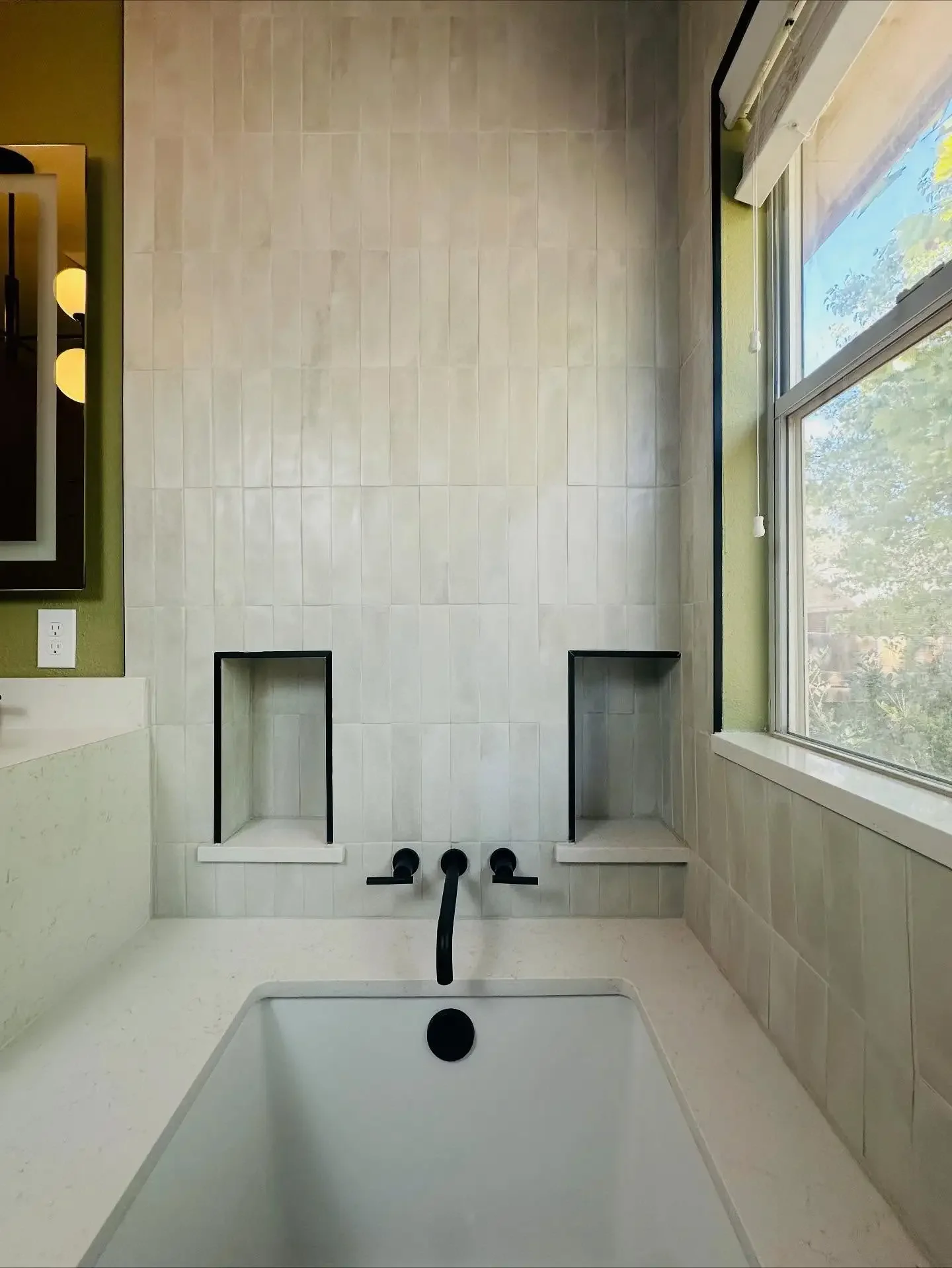 Empty bathroom with built-in shower niches, a large window, and a bathtub with black fixtures.