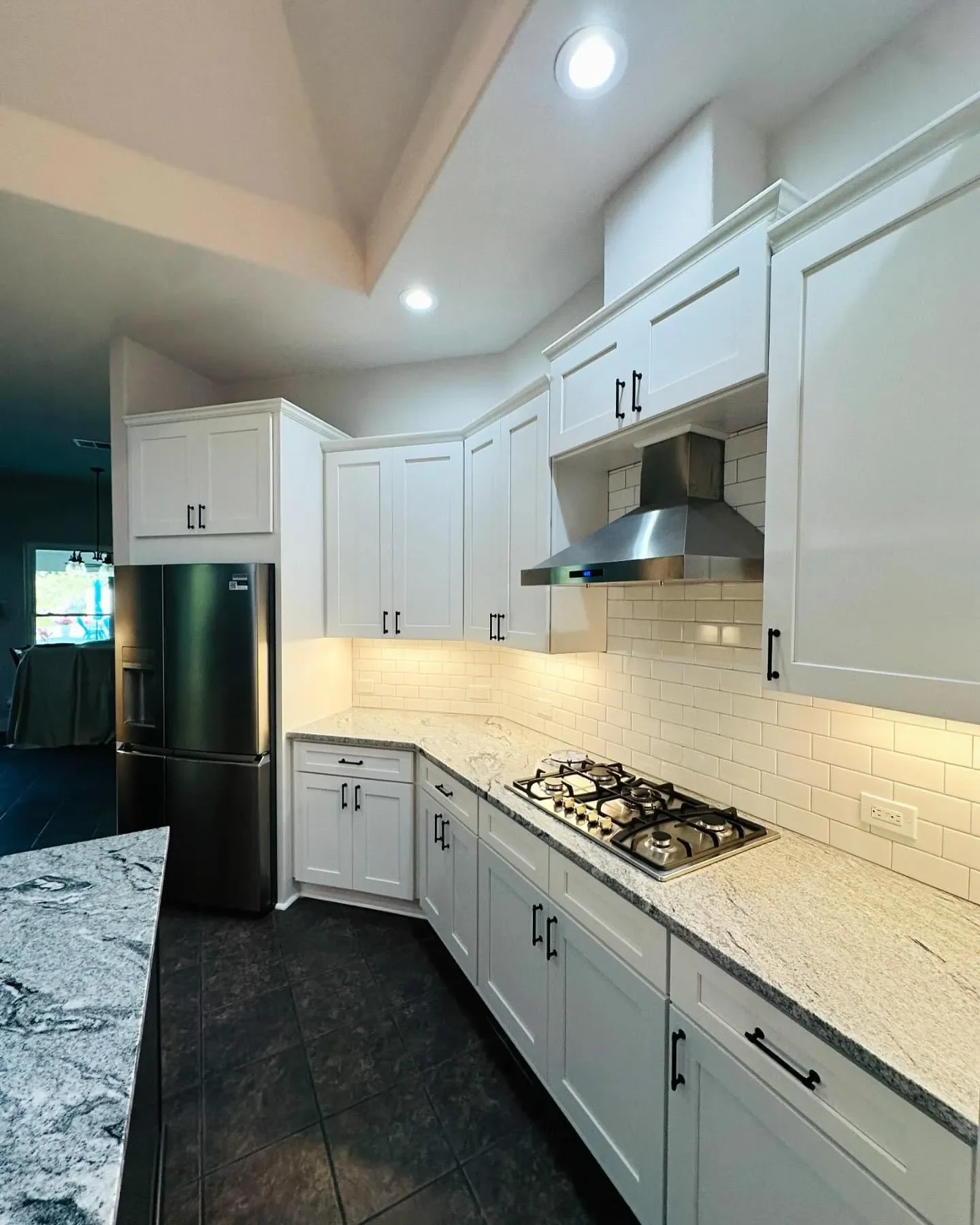 Modern kitchen with white cabinets, granite countertops, stainless steel appliances, and a gas stove beneath a stainless steel range hood.