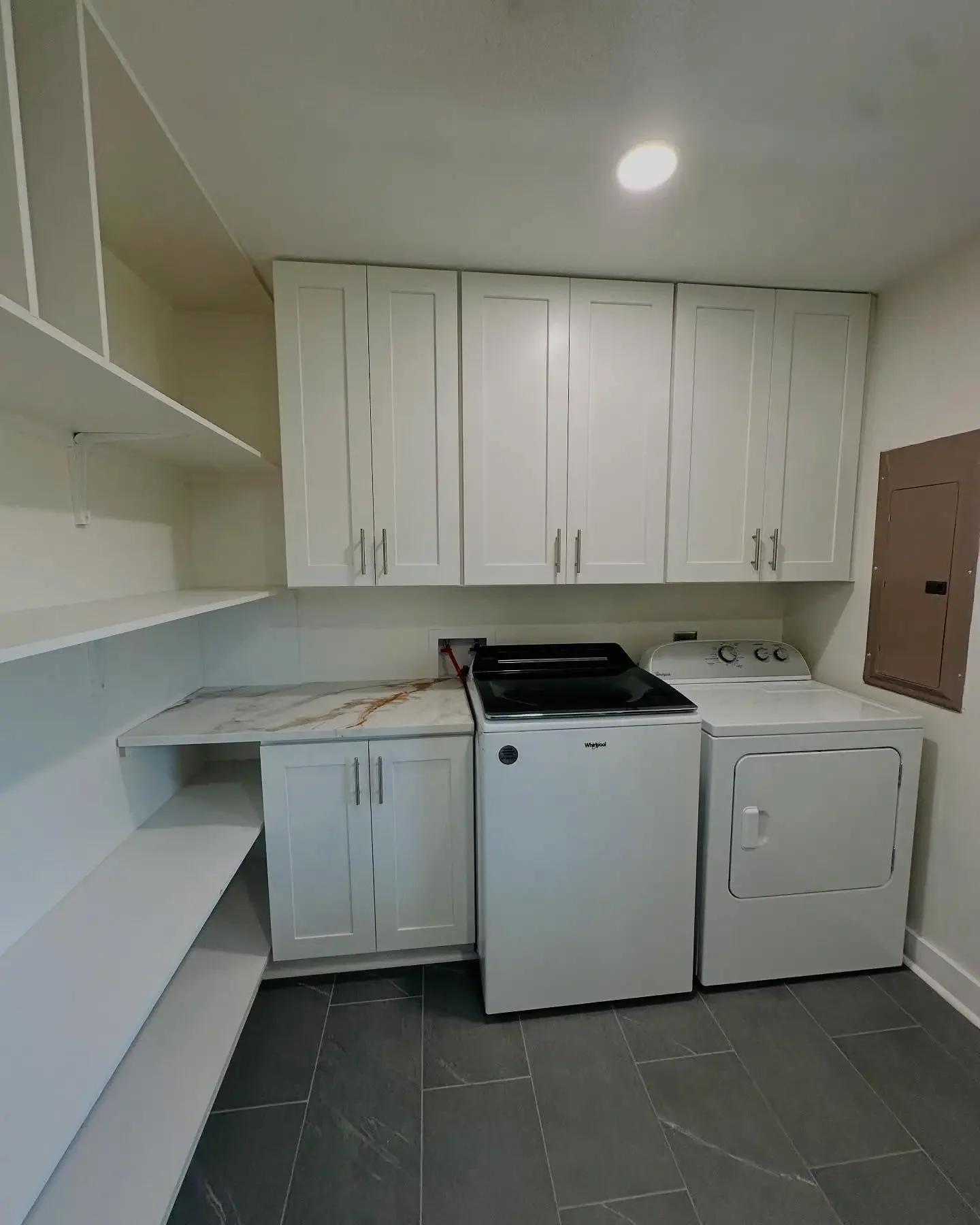 Laundry room with white cabinets, a washing machine, a dryer, tiled floor, and a small counter with marble pattern surface.
