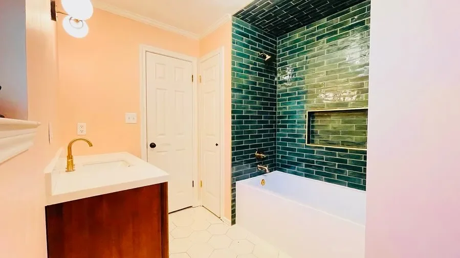 Bathroom with peach walls, white sink with gold faucet, green tiled shower area, and white bathtub.