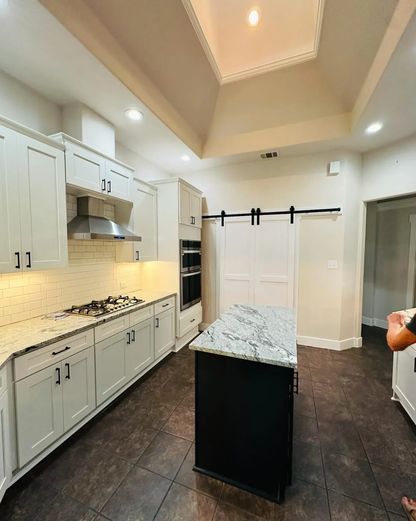 Modern kitchen with white cabinets, granite countertops, a stainless steel range hood, and a black island with a marble countertop.