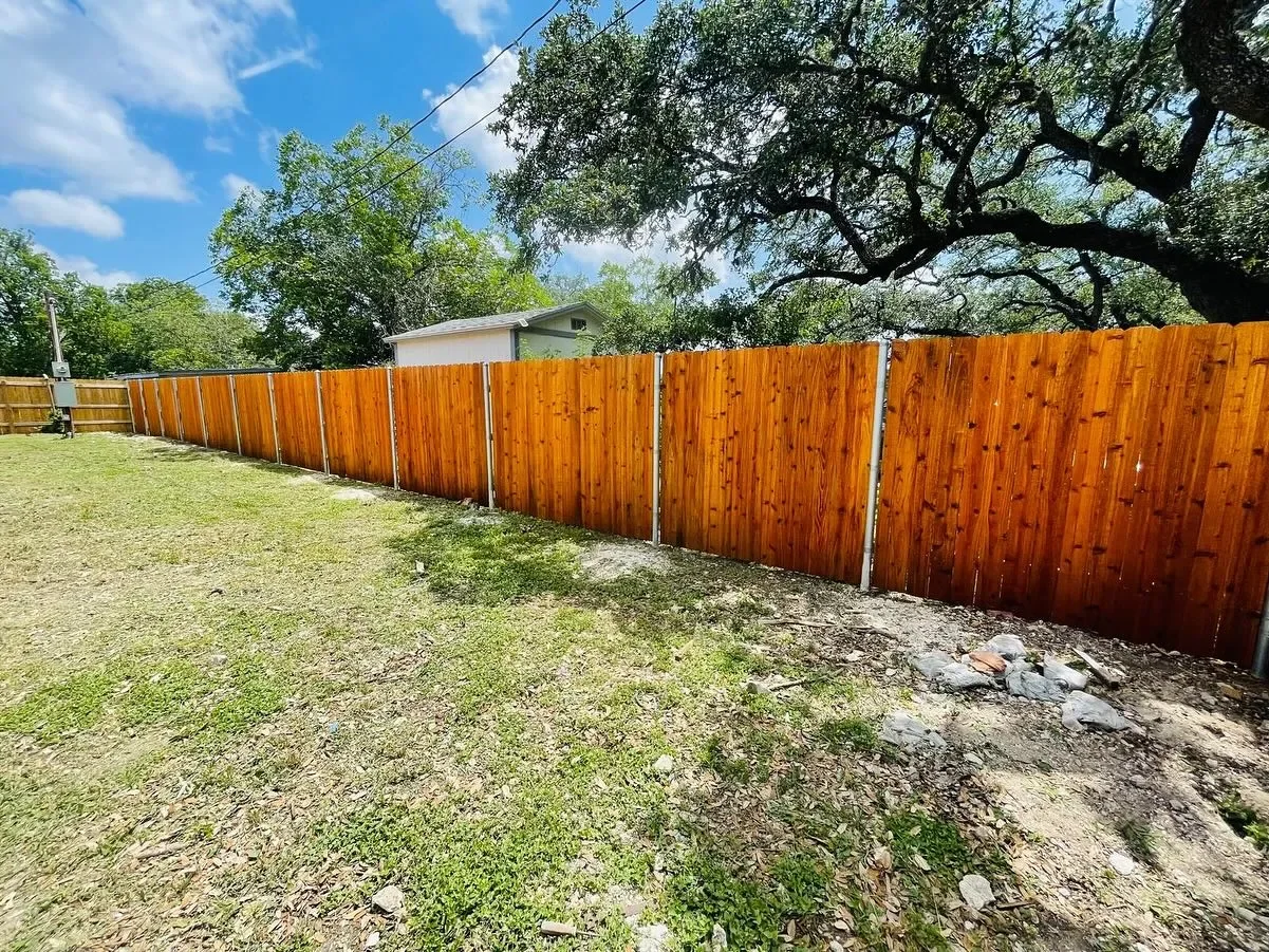 New wooden privacy fence installed along backyard, with green grass and trees under a partly cloudy sky.