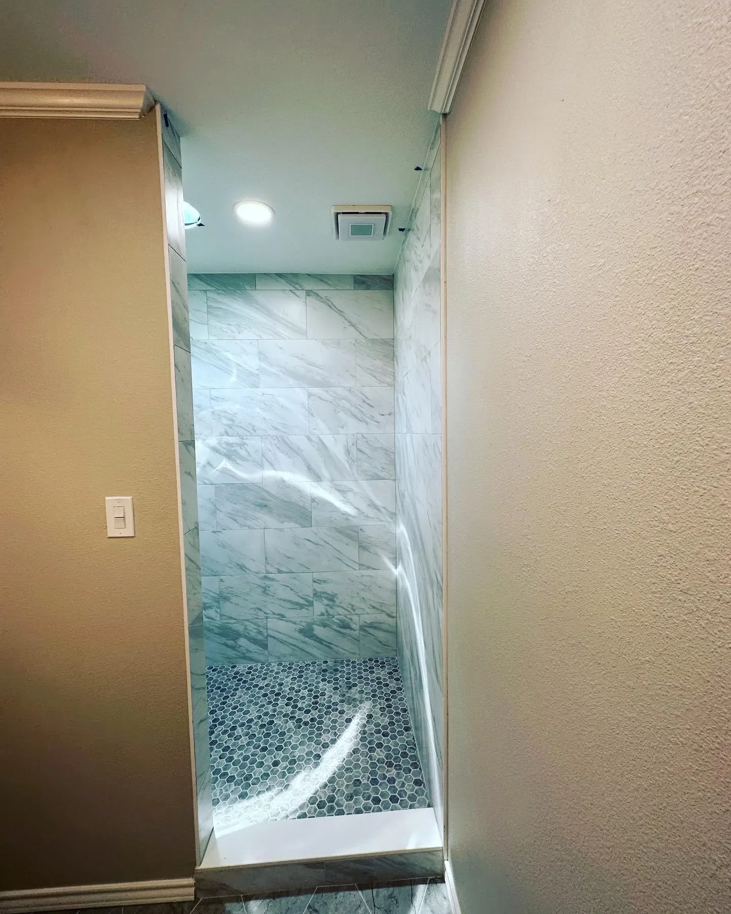Visible shower with marble tile walls, dark hexagonal tile floor, and ceiling-mounted exhaust vent.