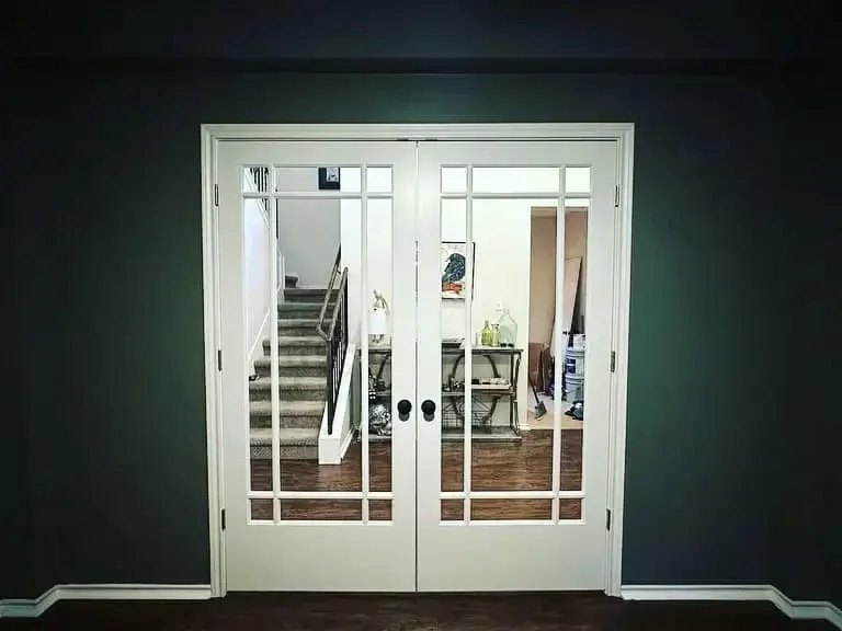 Interior view of a room with white double glass doors, dark walls, and a staircase in the background.