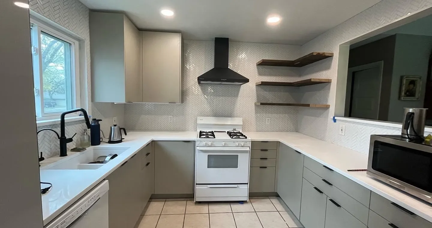 Kitchen with white cabinets, a white stove, open wooden shelves, a microwave, black kettle, and a window with a view outside.