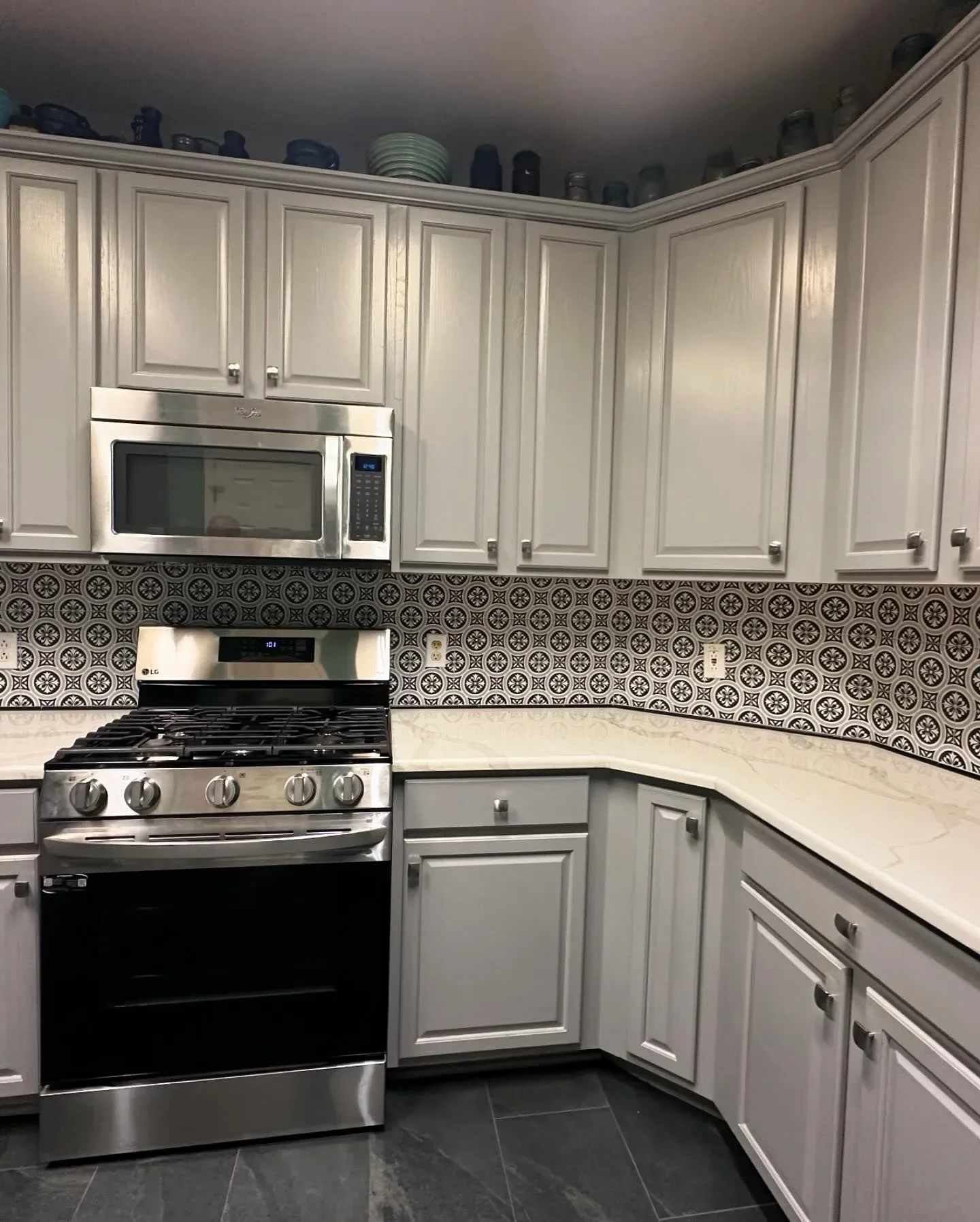 Kitchen with gray cabinets, patterned backsplash, stainless steel microwave, stove, and black tiled floor.