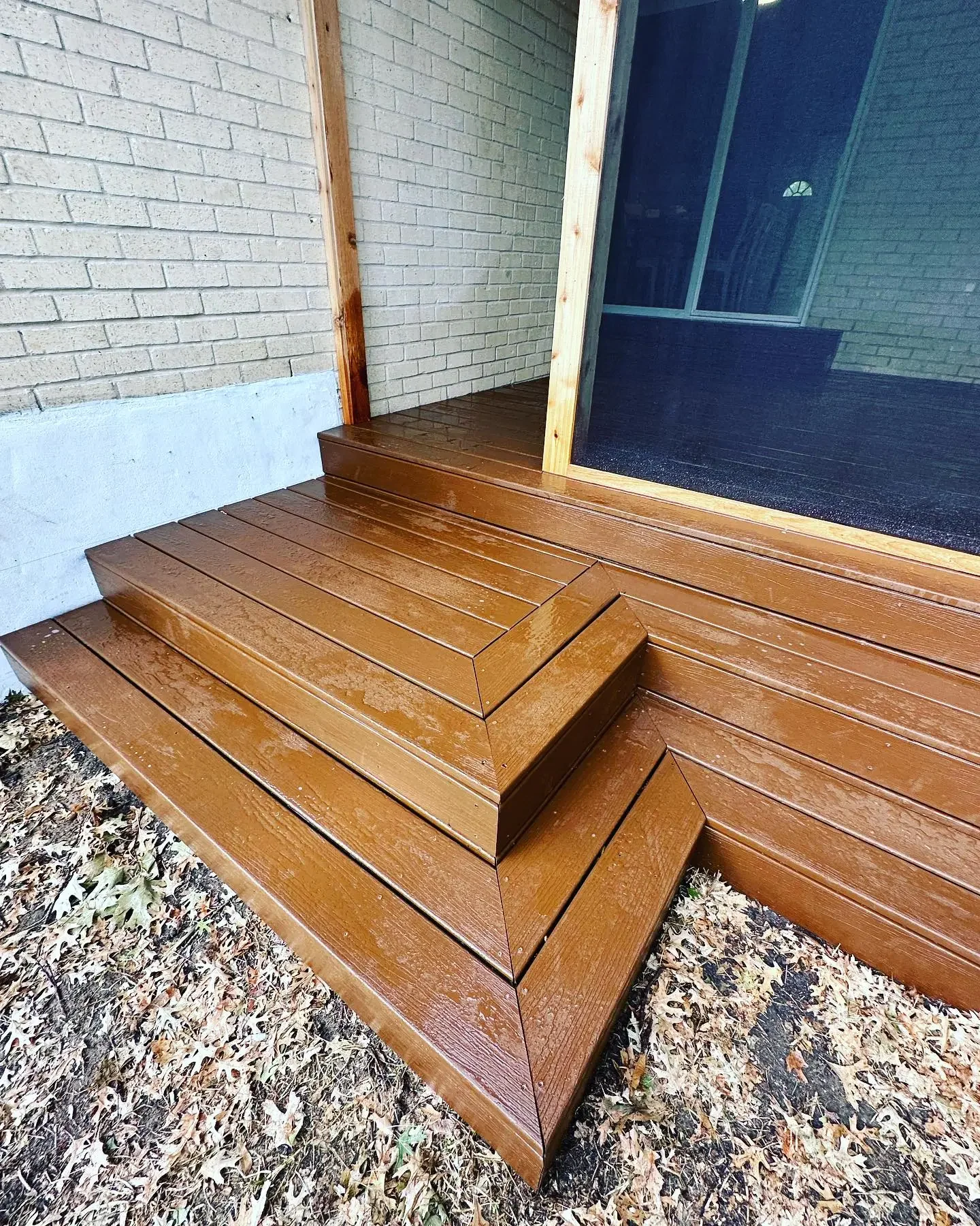 Wooden deck with stairs outside a house, next to a sliding glass door.