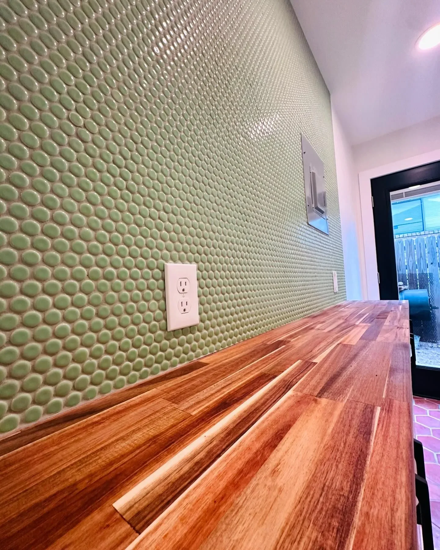 Close-up of a kitchen or bar counter with a green tiled backsplash and a white electrical outlet.