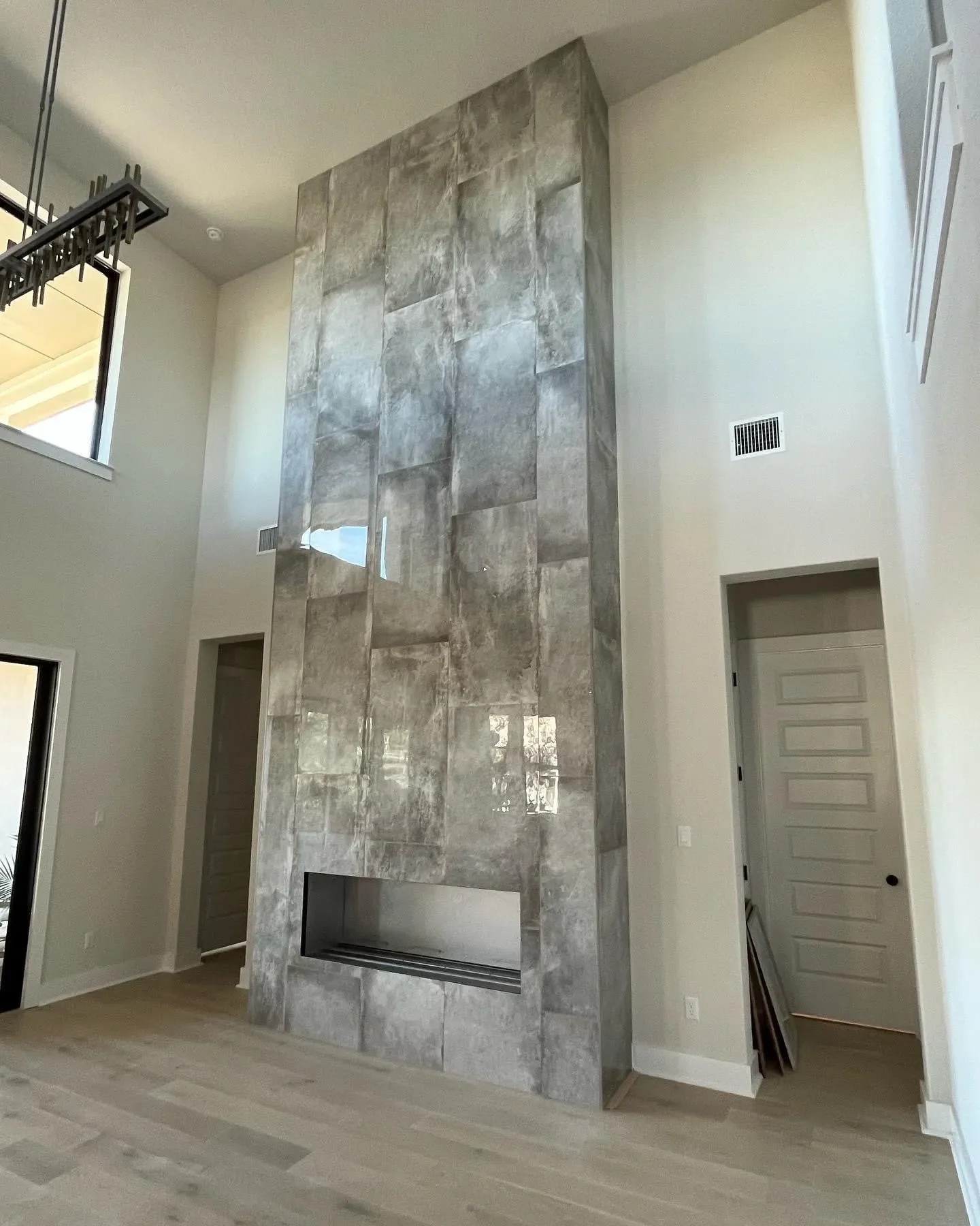 Modern living room with large decorative stone fireplace, high ceilings, light-colored hardwood floors, and large windows providing natural light.