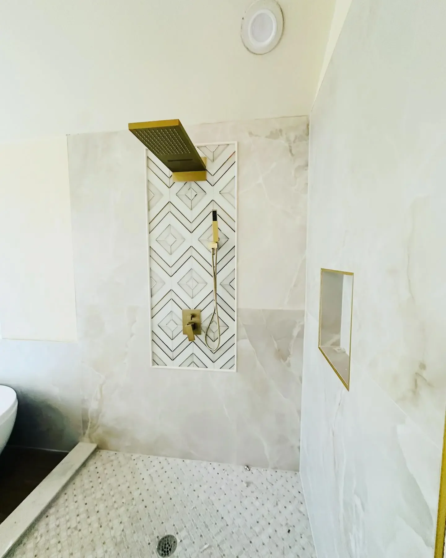 Modern shower with gold fixtures, a large rainfall showerhead, a built-in niche, and marble-like tiles.
