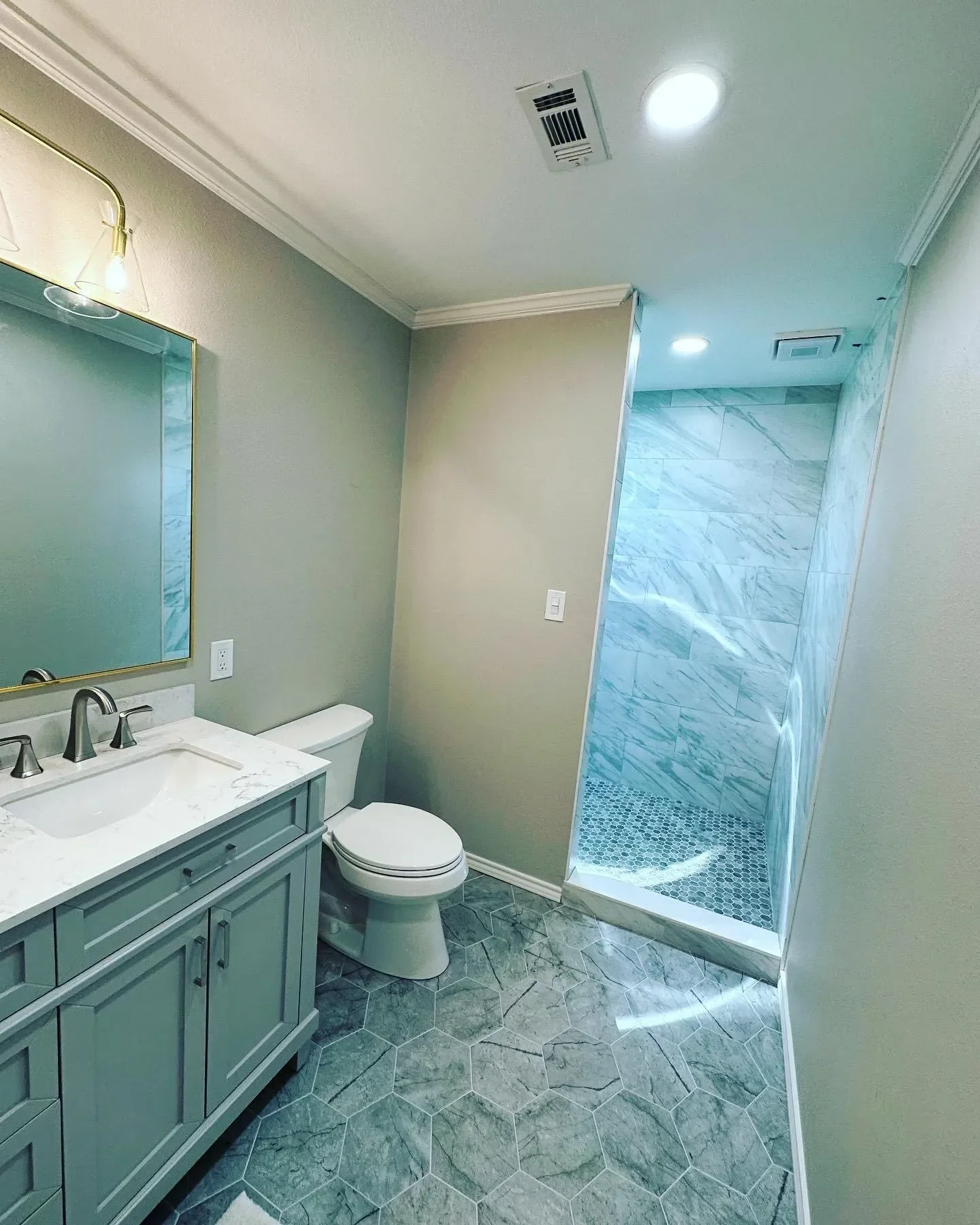 Bathroom with a vanity, mirror, toilet, and open shower with marble tiles and hexagonal floor tiles.