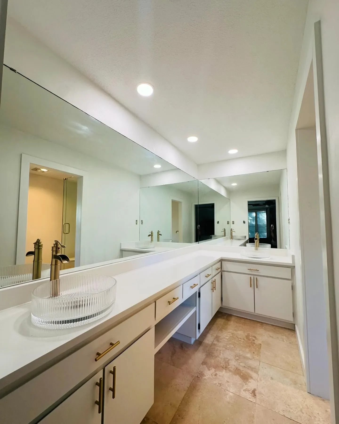 Bathroom with white countertop, gold faucets, large mirror, and beige tiled floor.