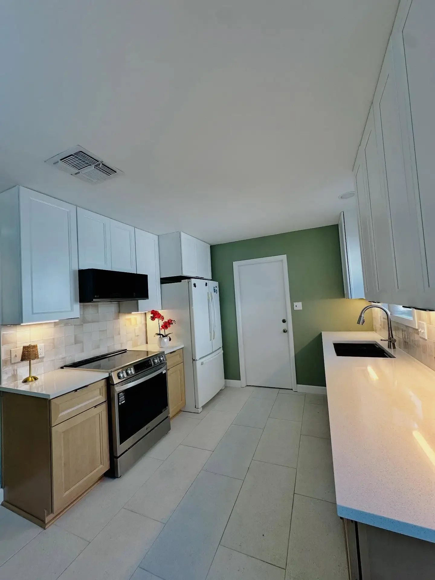Kitchen with white cabinets, beige countertop, stainless steel oven, black vent hood, white refrigerator, green accent wall, white door, and a window above the sink.