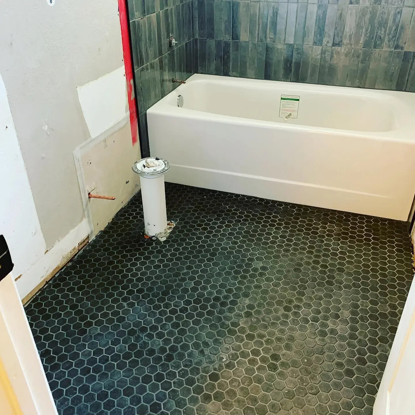 Bathroom under renovation with a black hexagonal tile floor, a white bathtub, and unfinished walls.