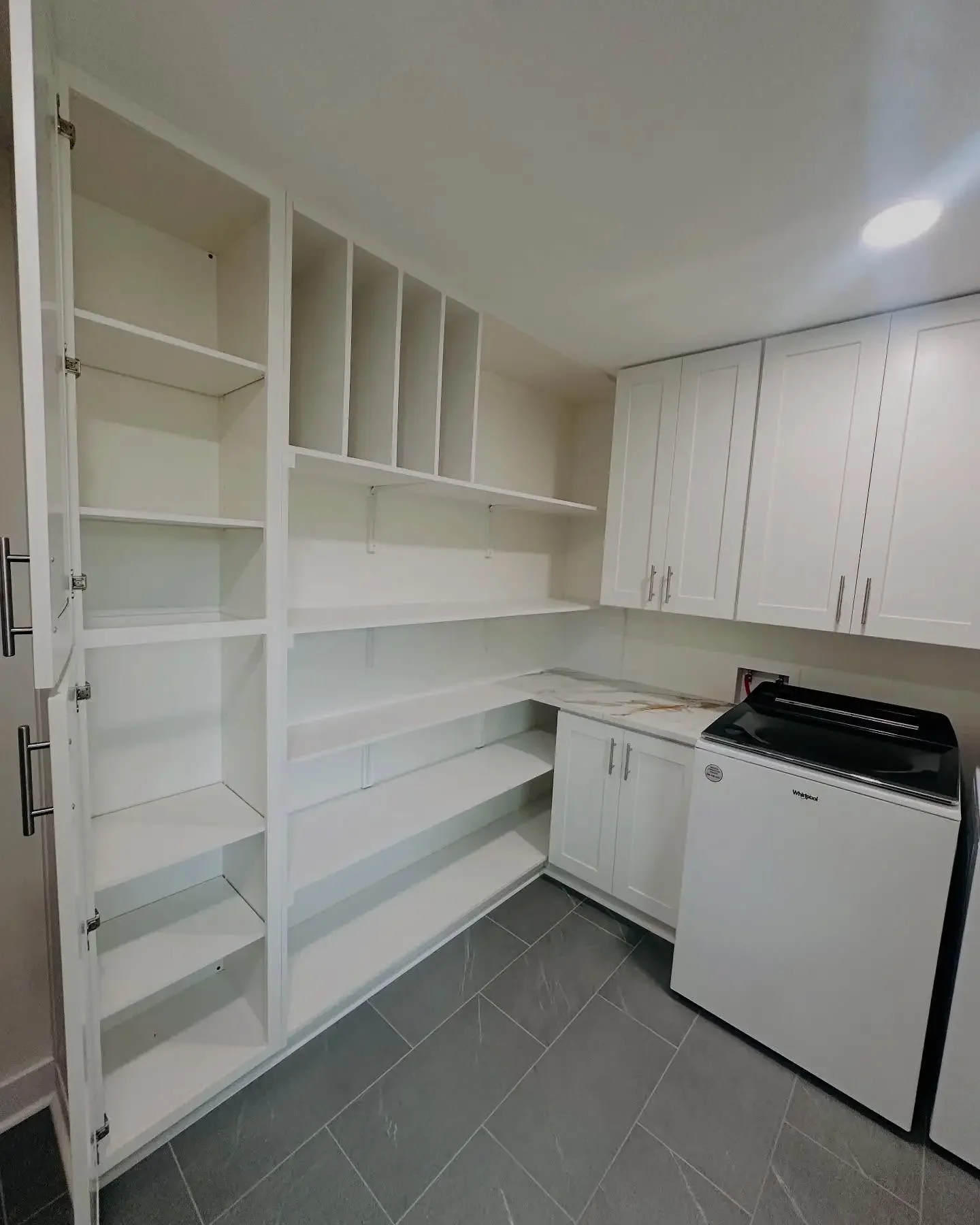 Empty kitchen with white cabinetry, open and closed shelves, and a washing machine in a modern, clean style.