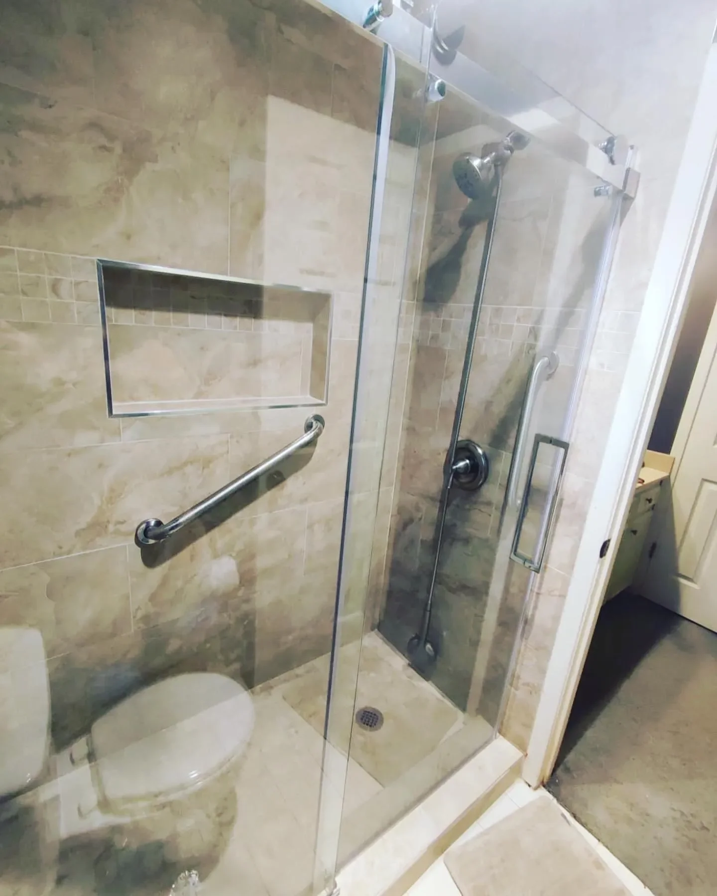 A walk-in shower with glass doors, beige tiled walls, a built-in wall niche, and a metal grab bar.