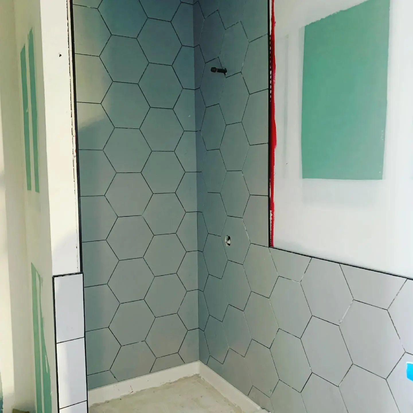 Partially finished bathroom with hexagon tile wall and mirror, unfinished shower area with visible plumbing and construction materials.