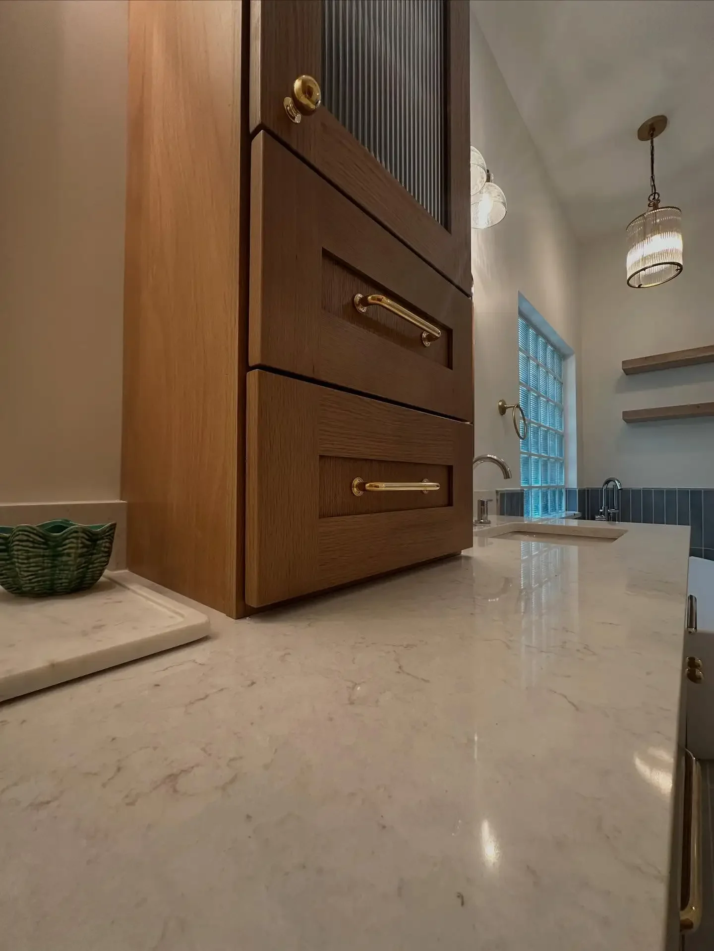 Close-up of a kitchen countertop with a wooden cabinet and a small green basket, a marble surface, and a small sink in the background.