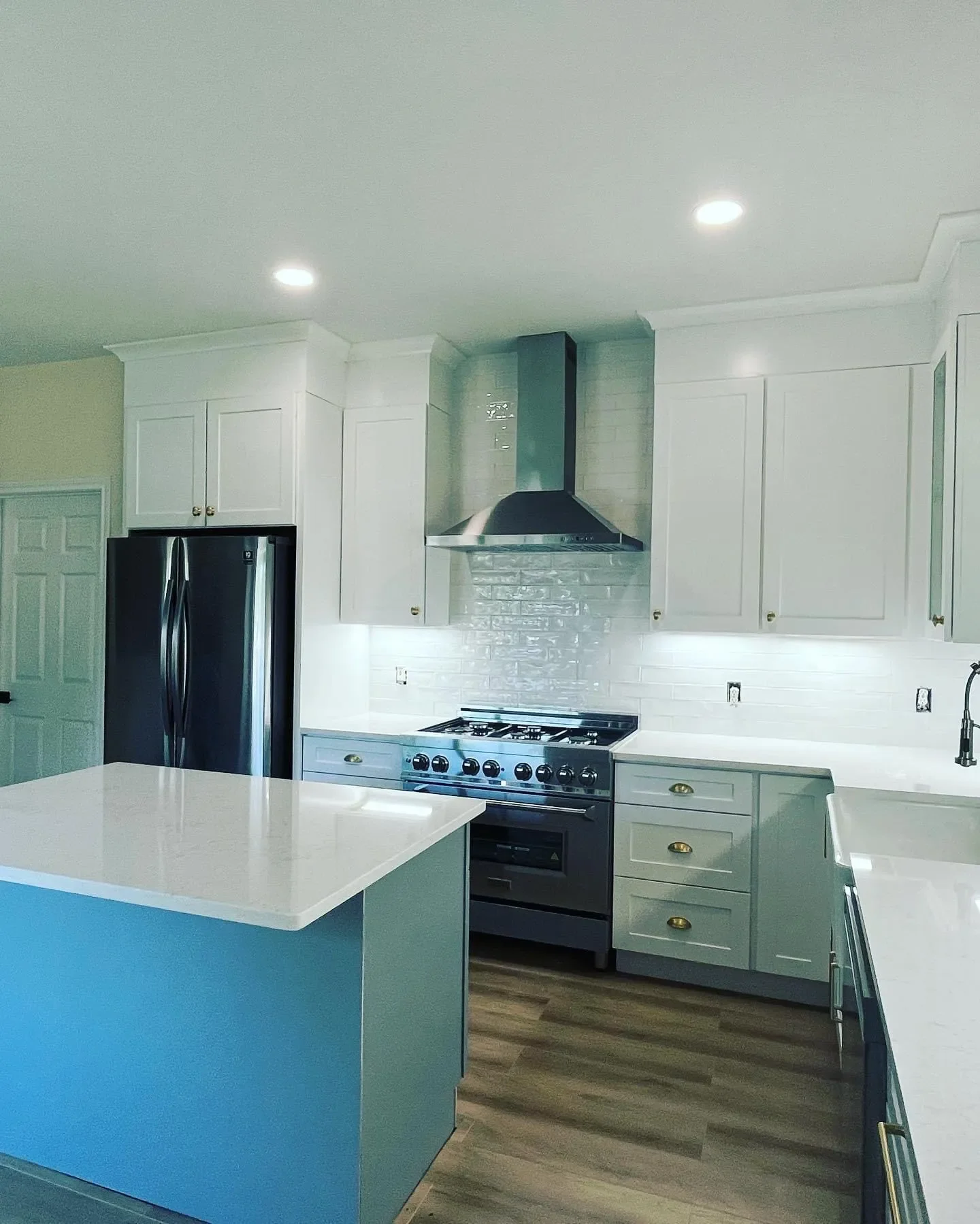 Modern white kitchen with black appliances, a center island with a white countertop, stainless steel range hood, and light wood floors.