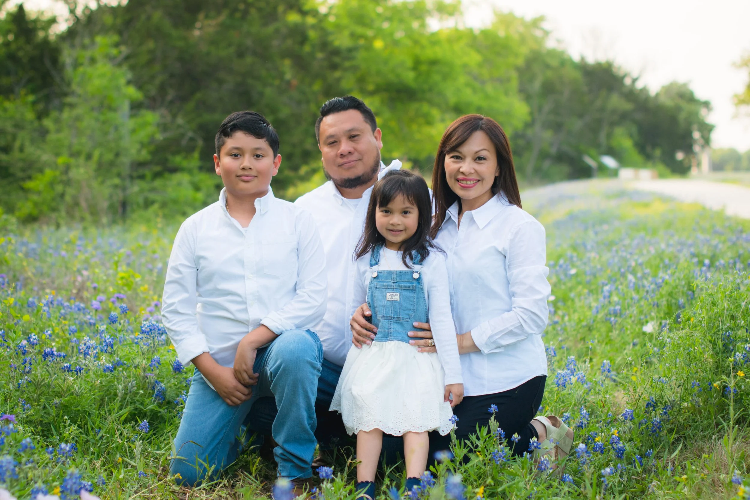 Family of five in a field of blue and purple flowers, with trees in the background, smiling for a photo.