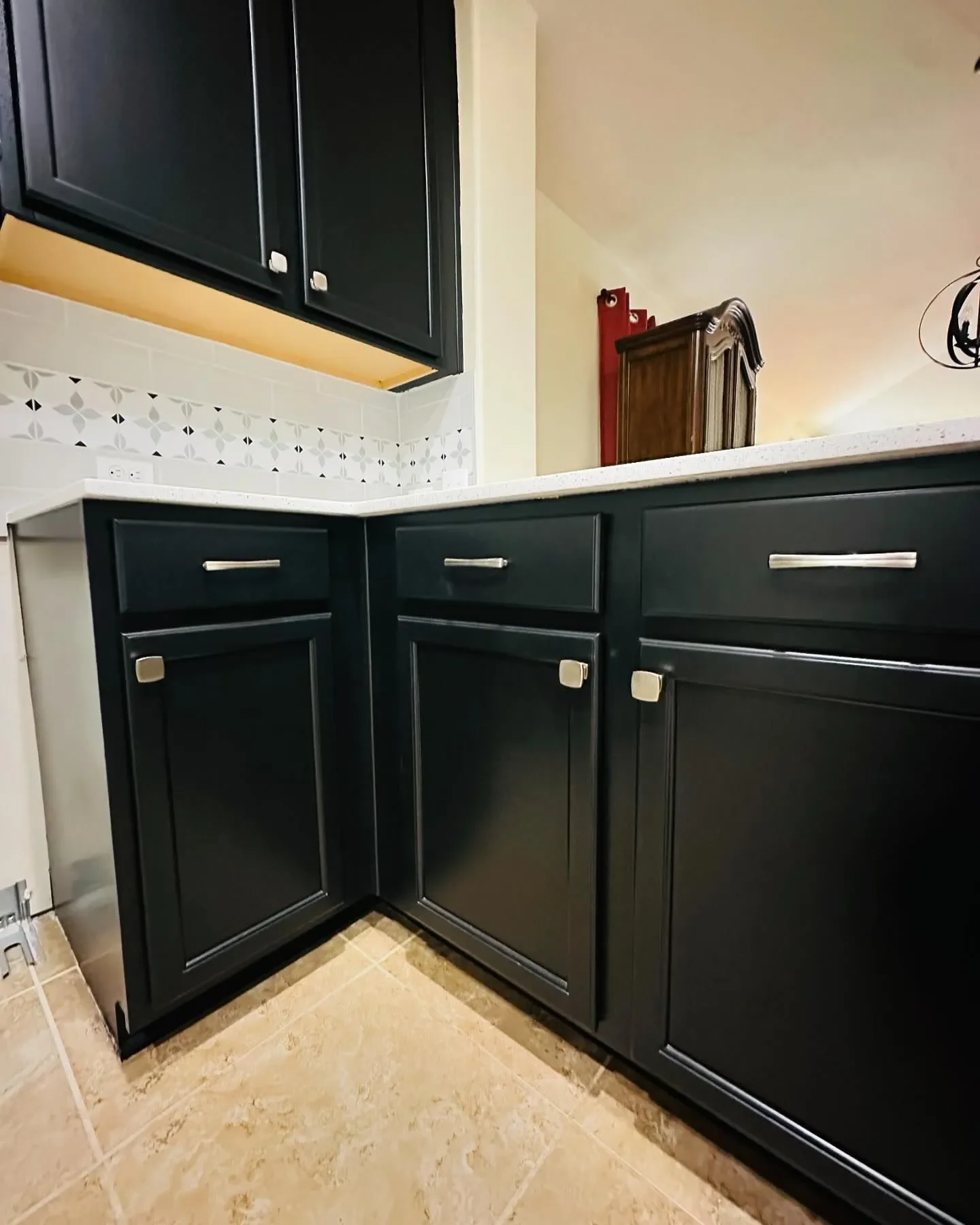 Close-up view of black kitchen cabinets with silver handles, white countertop, and beige tiled floor.