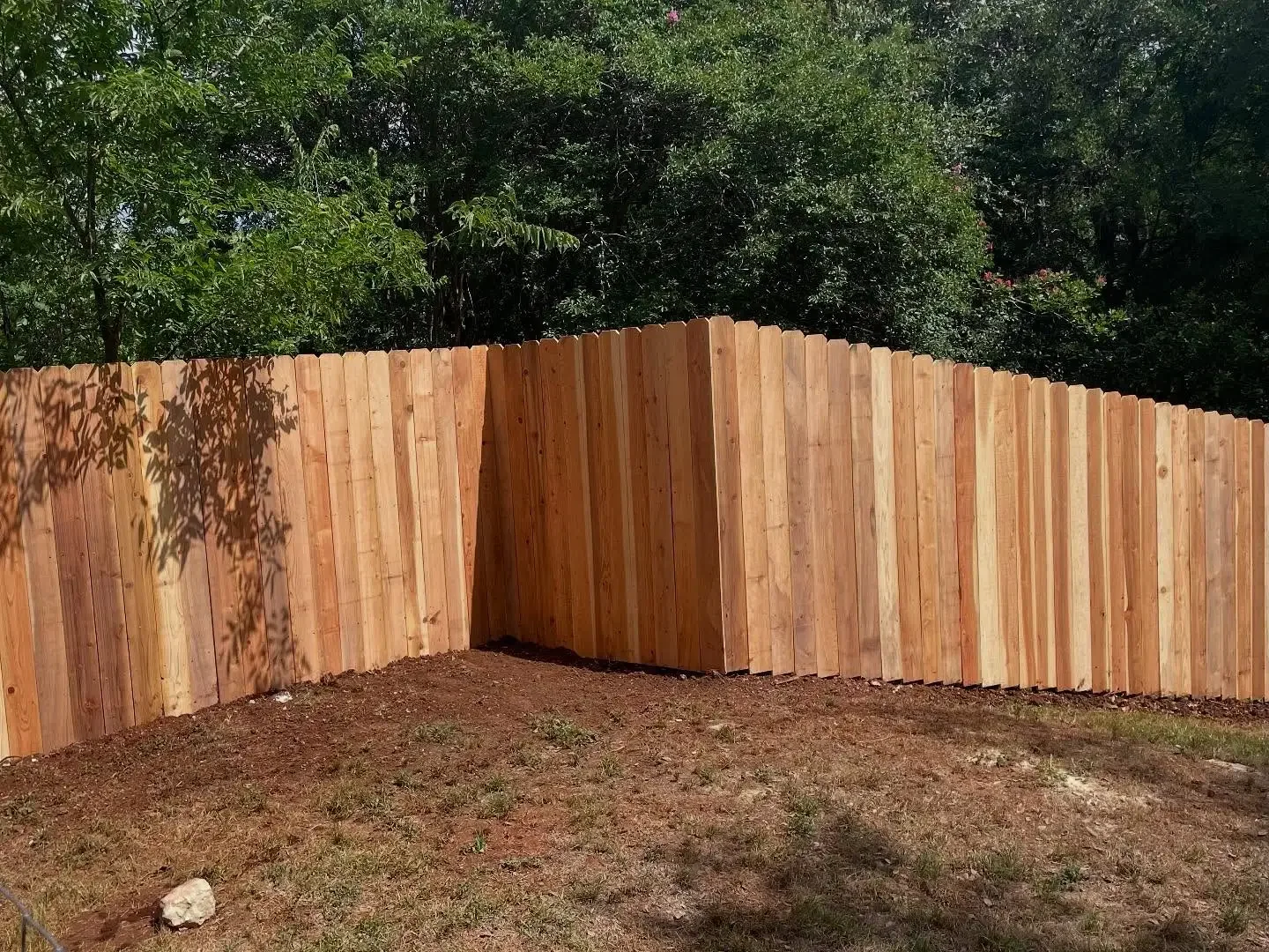 A wooden privacy fence in a yard, with trees and greenery in the background.