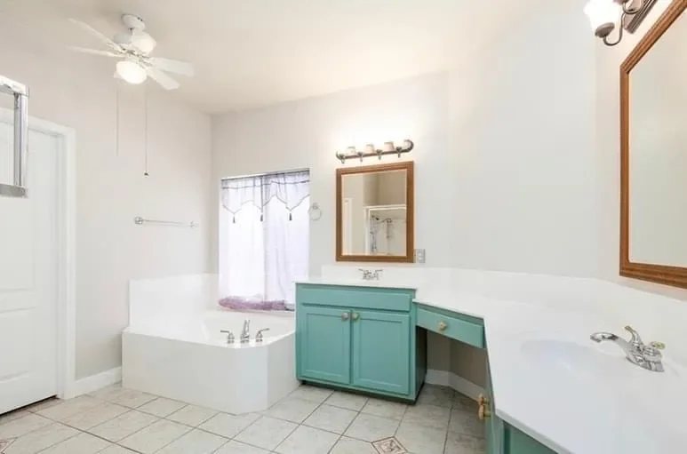 Bathroom with white walls, a bathtub with a purple curtain, two mirrors with wooden frames, a teal vanity with a bowl sink, tiled floor, and a ceiling fan.