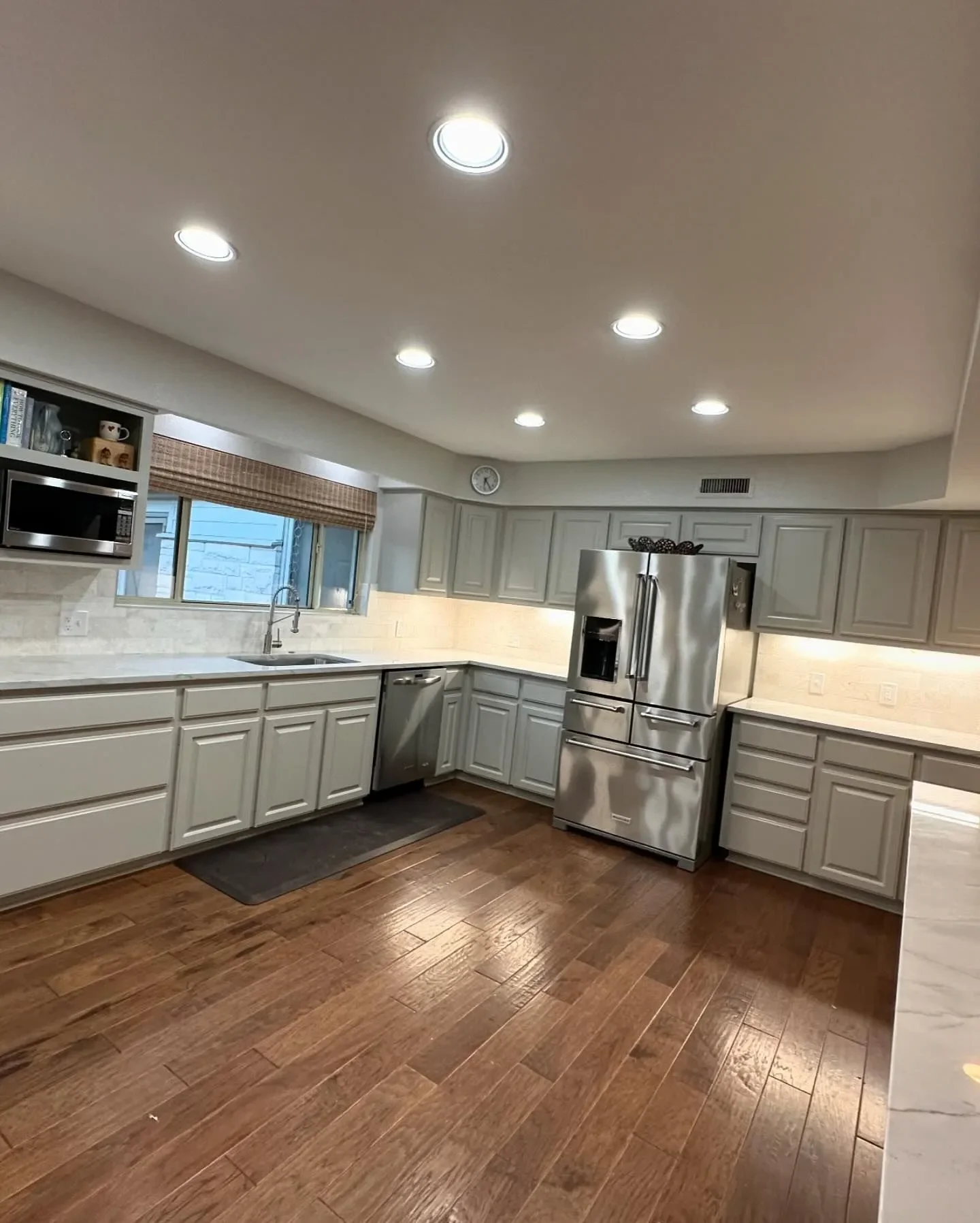 Modern kitchen with white cabinets, stainless steel refrigerator, microwave, and a window above the sink.