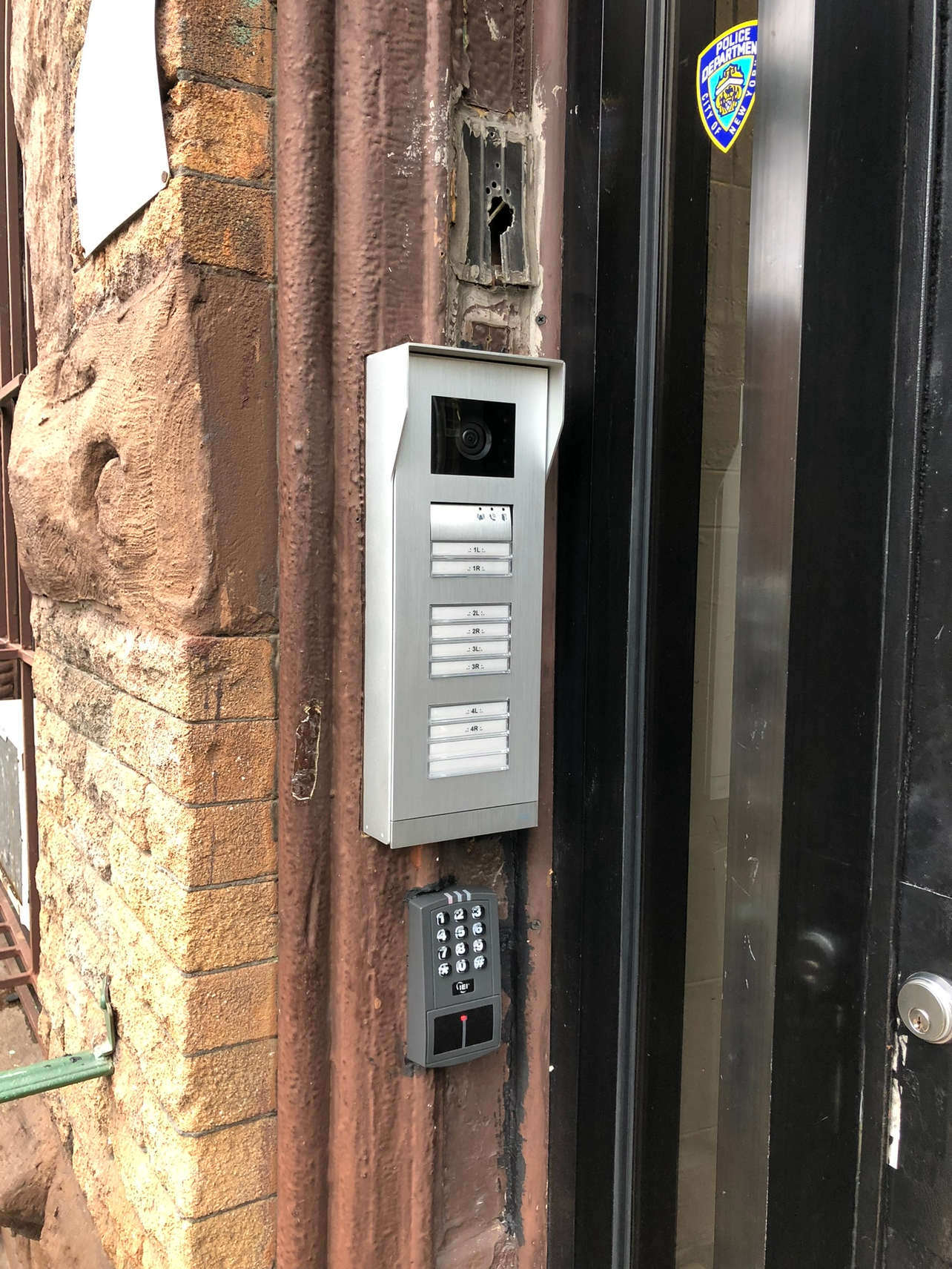 Apartment building buzzer intercom system and overhead security camera mounted on a brick entrance wall.