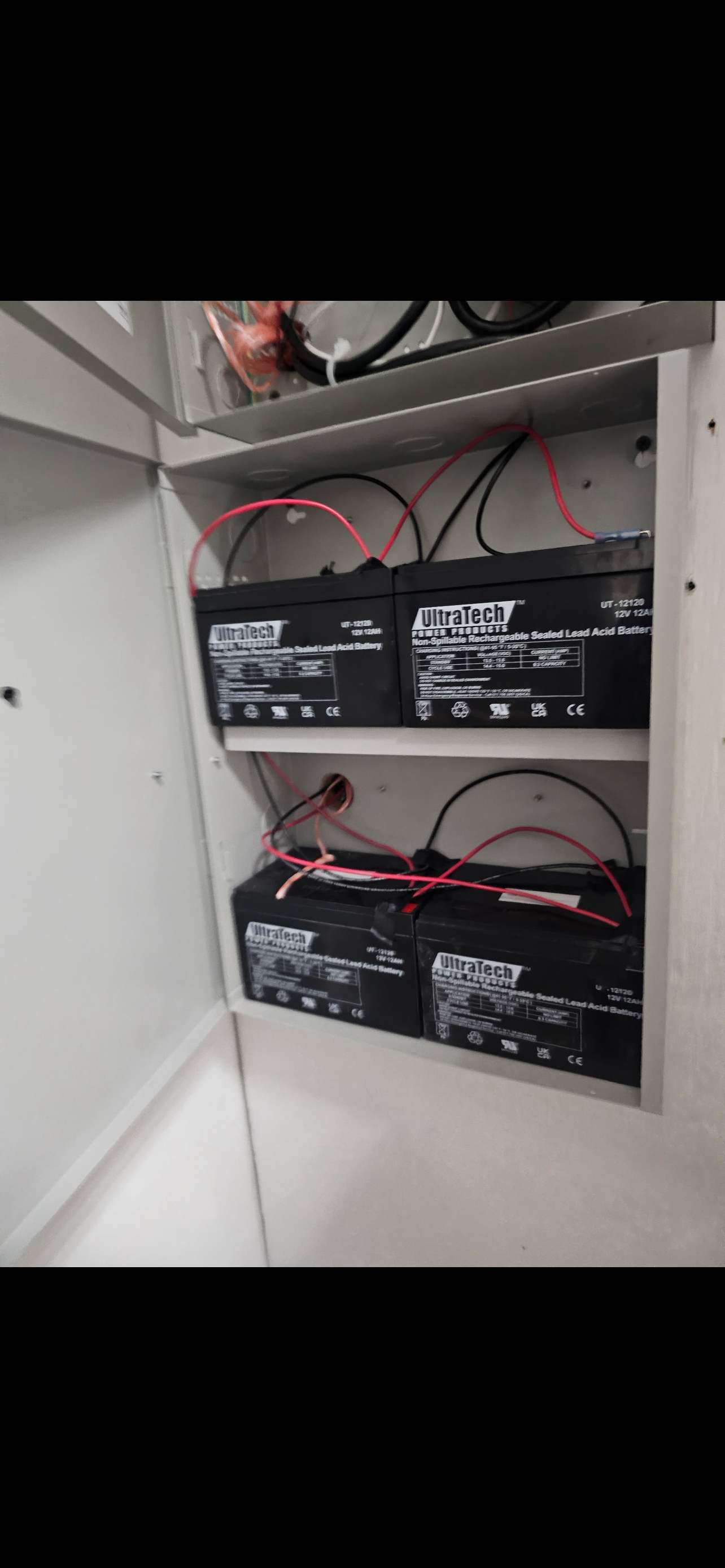 Three black sealed lead-acid batteries labeled UltraTech inside an electrical panel with connected red and black wires.