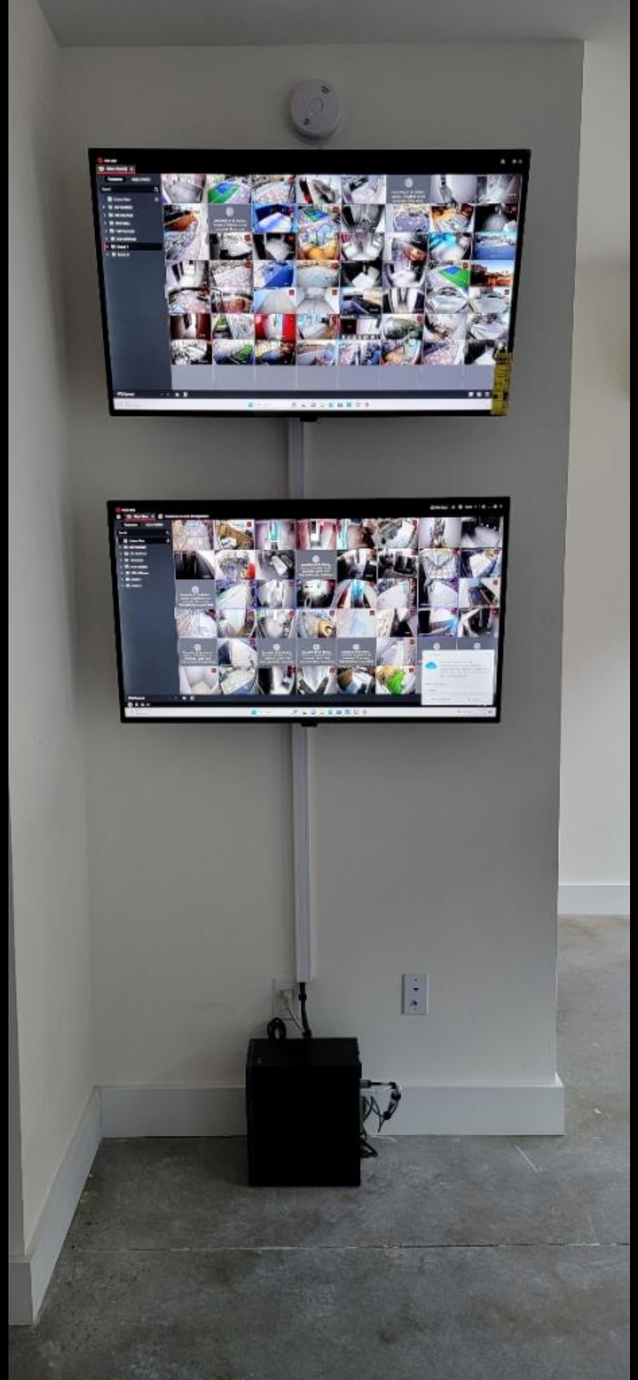 Two wall-mounted monitors displaying surveillance camera footage in an indoor setting - Impera Security Systems. 