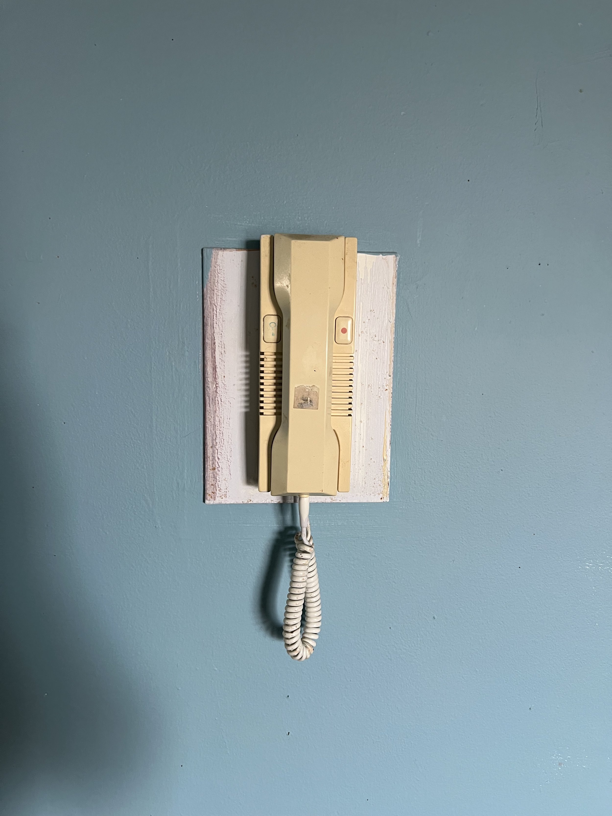 A beige rotary landline telephone mounted on a white wooden board on a light blue wall.