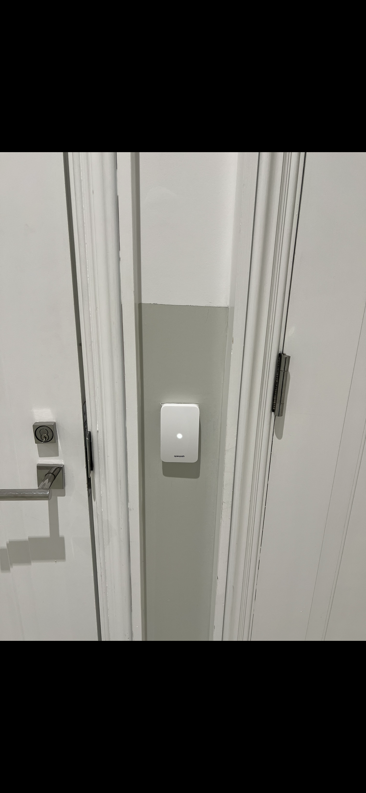 A doorway with a white door and a gray wall section with a white device mounted on it.