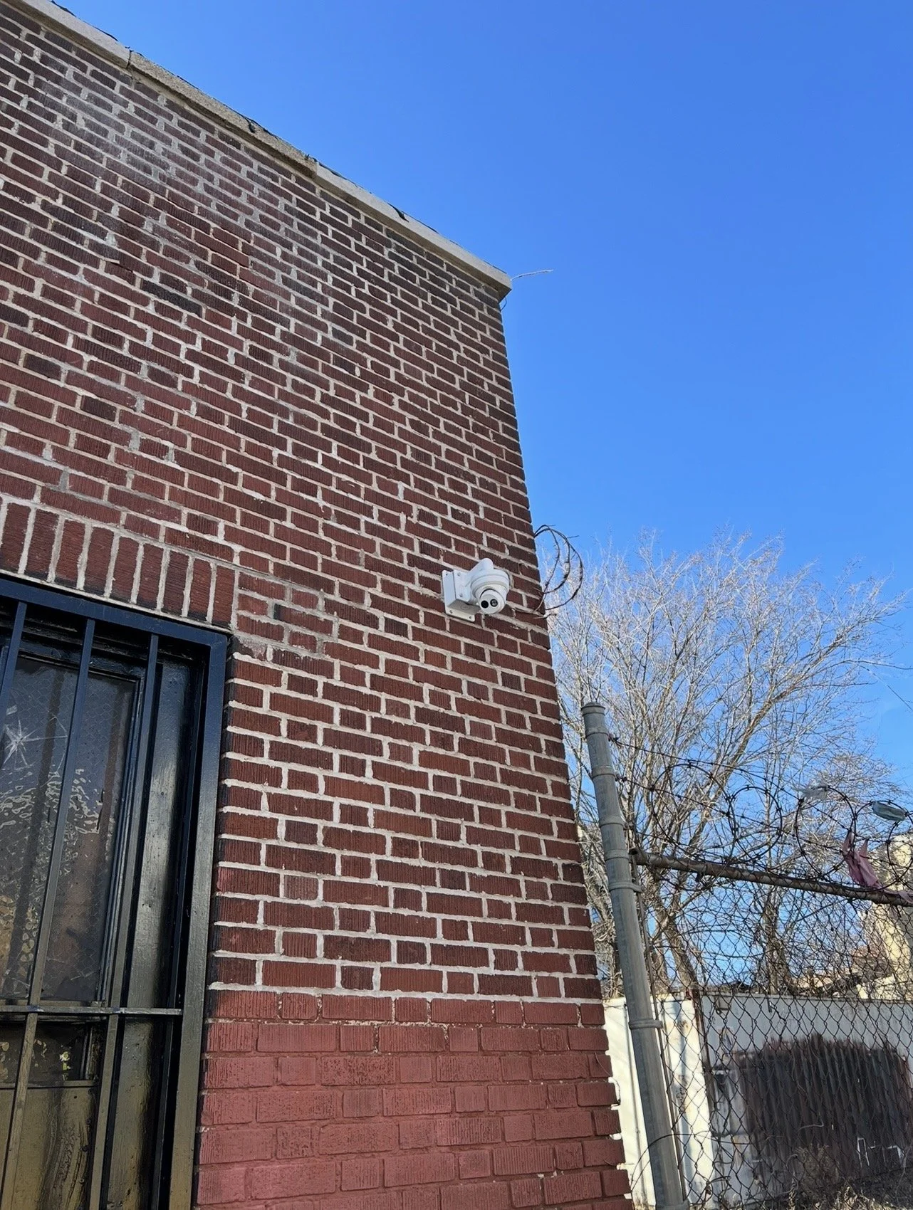 Close-up of a brick building corner with a security camera mounted on the wall and clear blue sky in the background.