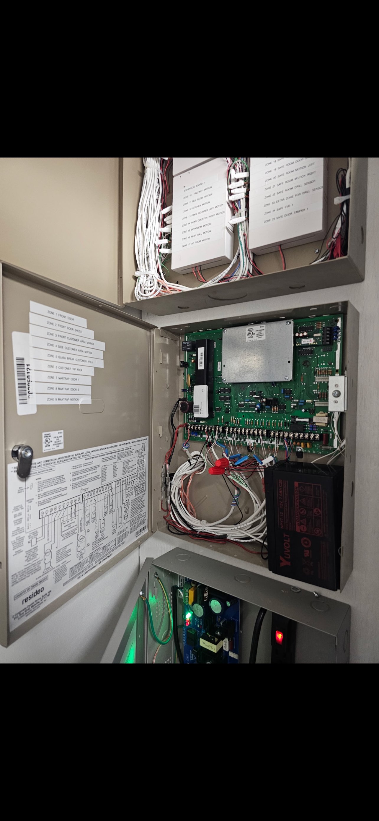 Open security control panel with internal circuit boards, wiring, and labels.