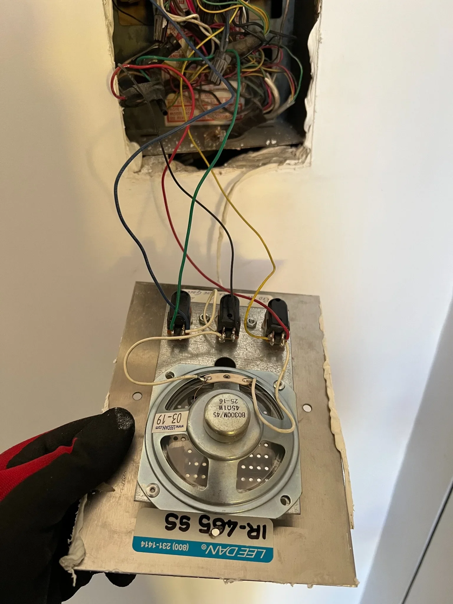 Lee Dan intercom speaker unit with its wiring exposed, resting on a Lee Dan box while a gloved technician holds it.