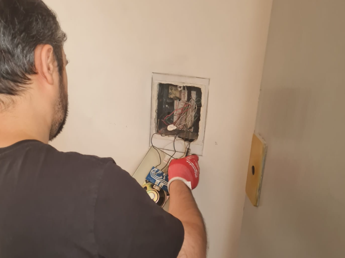 Man working on an electrical outlet with exposed wiring, wearing a red glove on his right hand.