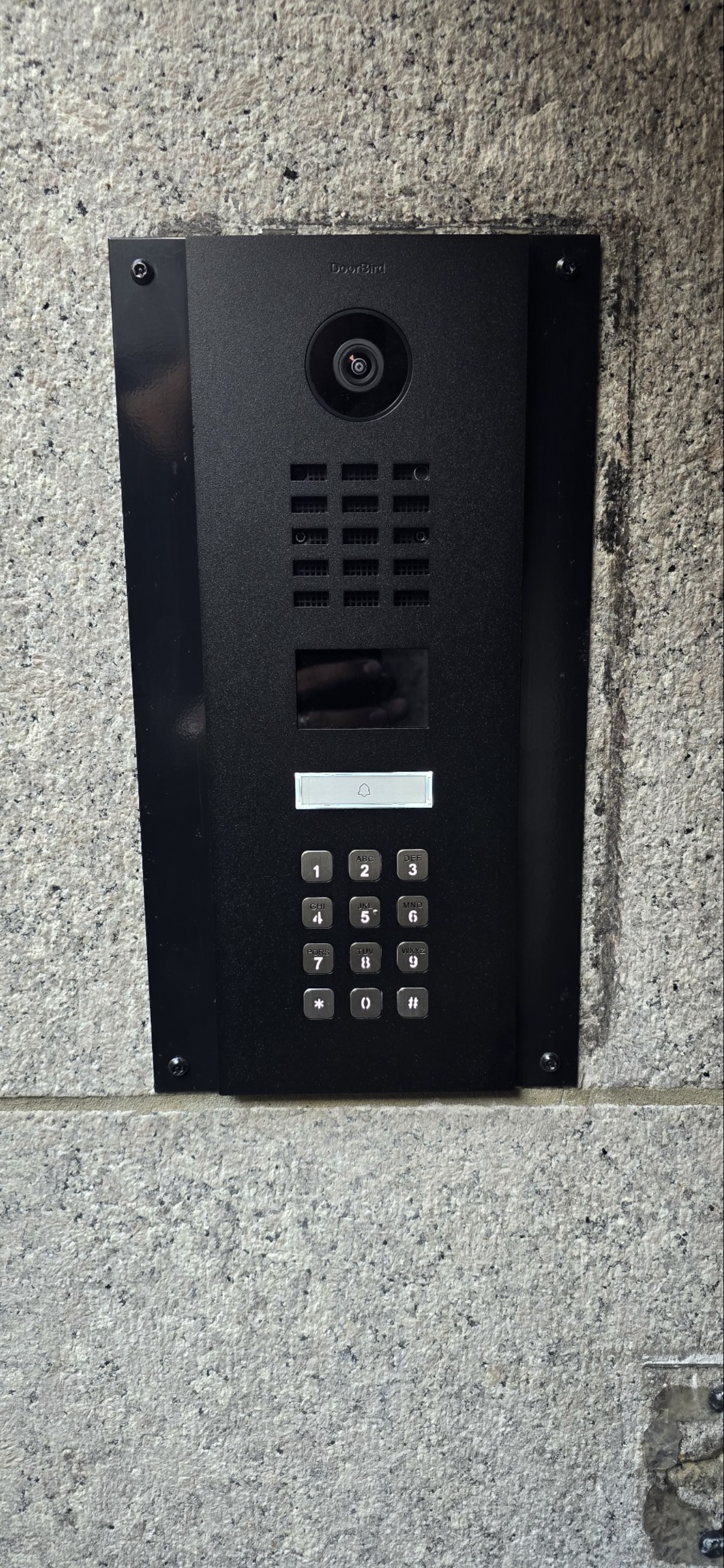Intercom and security camera mounted on a concrete wall, with a keypad for access.