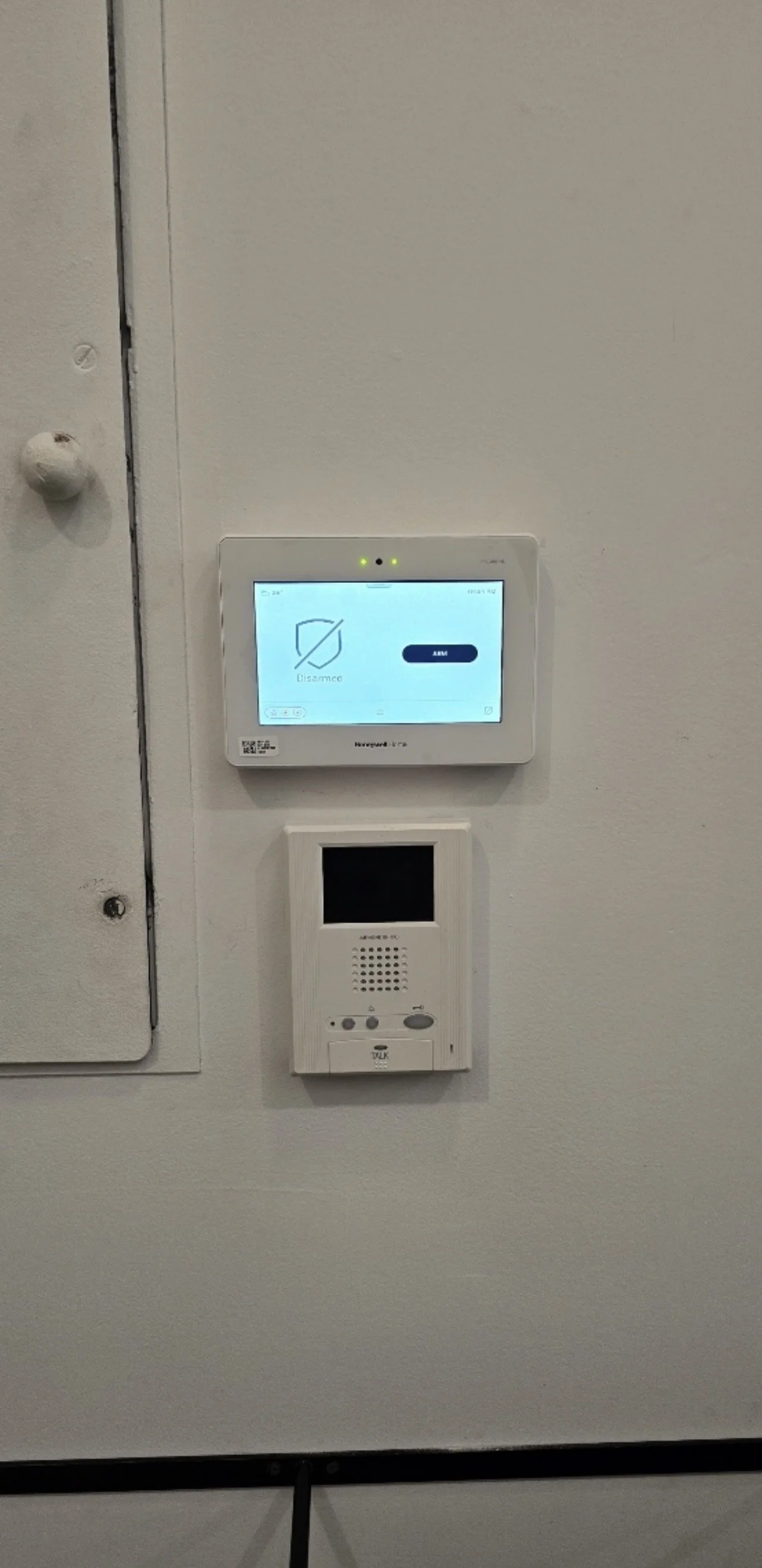 A wall-mounted security system with a touchscreen display and an intercom speaker below it.