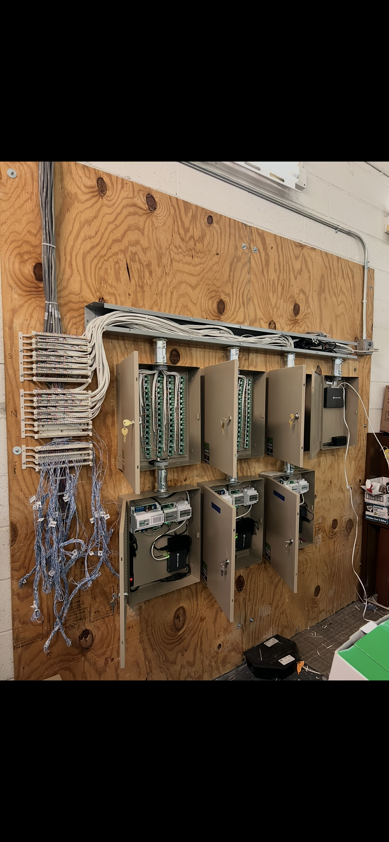 Electrical panels and wiring mounted on a plywood wall in an industrial or technical setting.