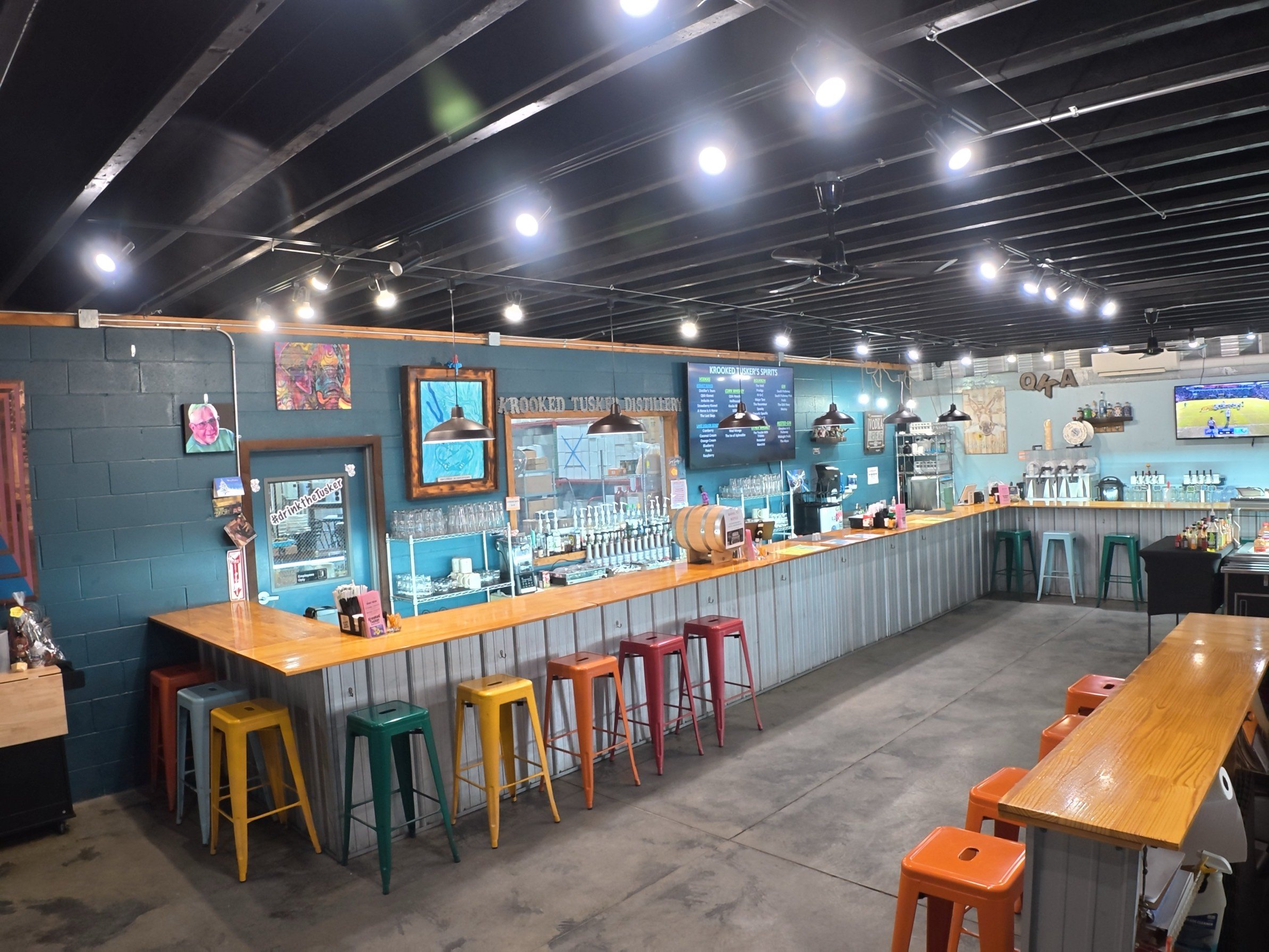 Empty bar area with colorful stools, TVs, and art on blue walls in a casual restaurant or bar.
