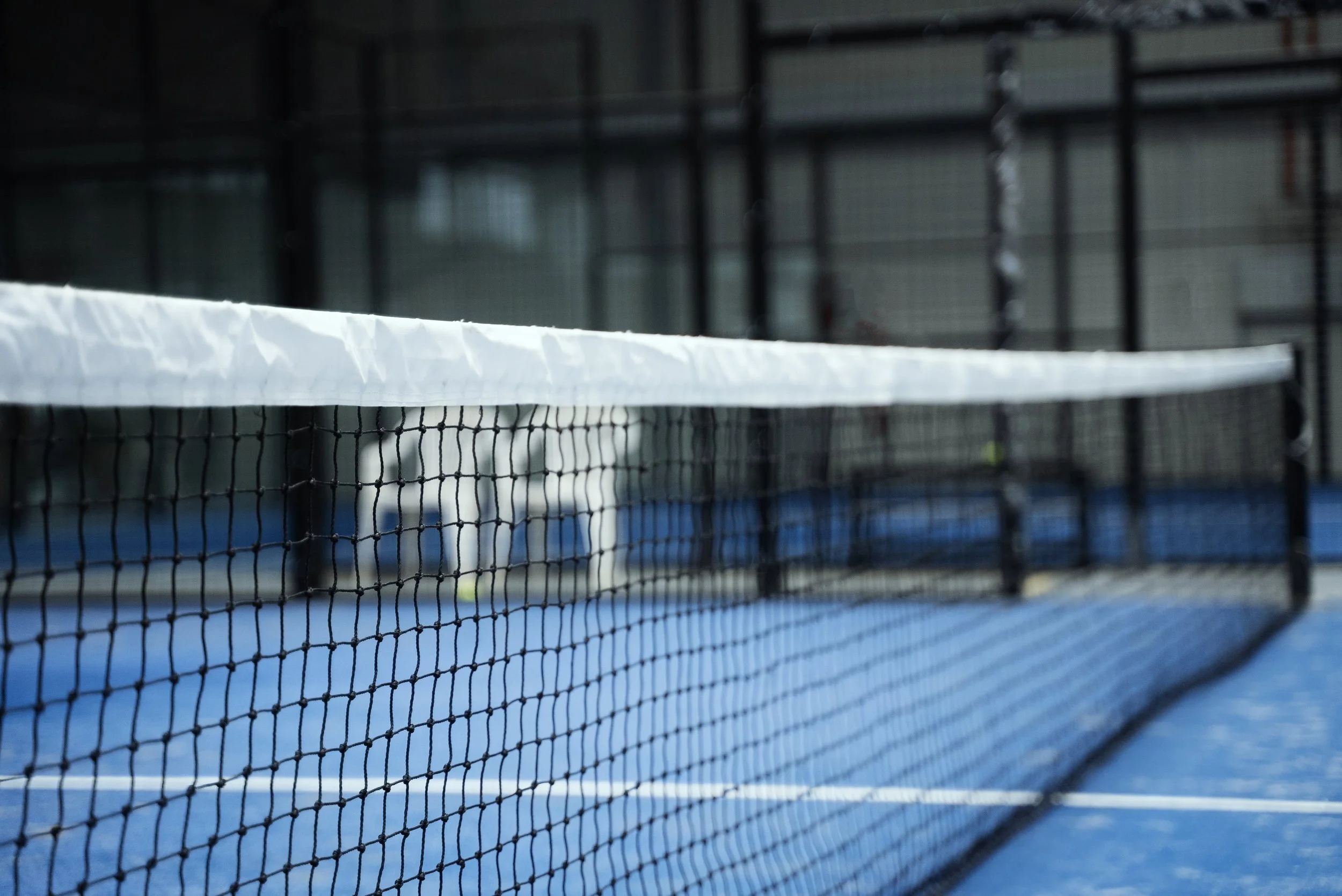 Close-up of a padel net on a blue court with a blurred indoor background.